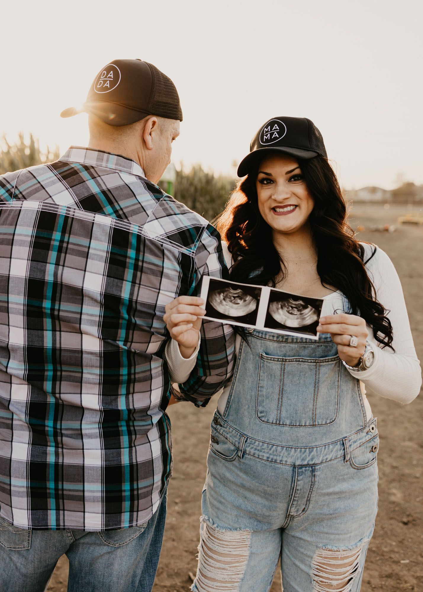 A couple sharing a moment while looking at ultrasound photos in a farm field setting.