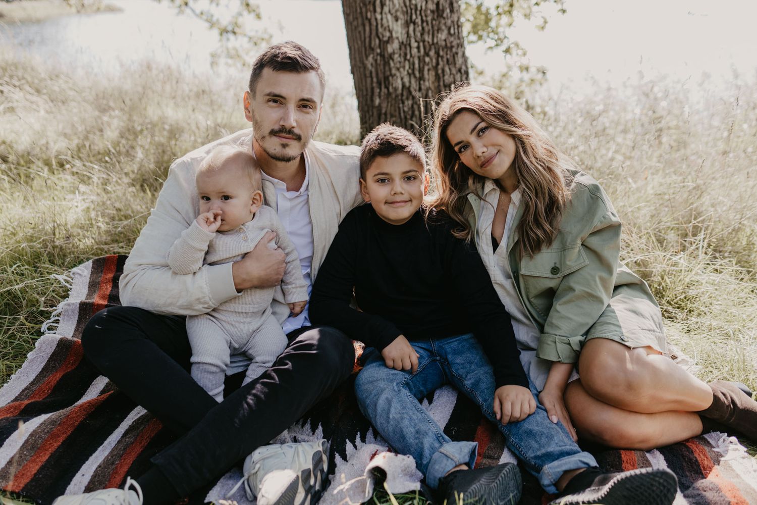 Family of four enjoying outdoor time together on a striped blanket under a tree.