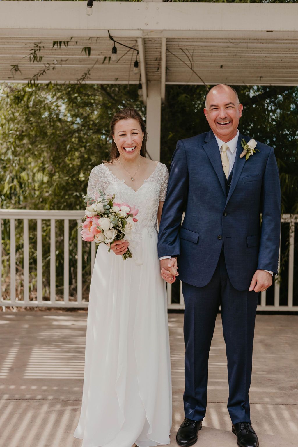 Happy couple poses for portrait on covered porch after wedding ceremony.