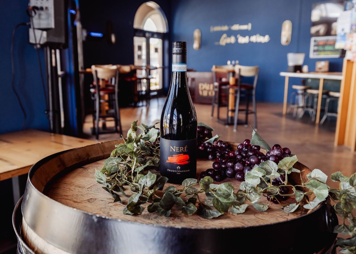 Restaurant interior with blue walls featuring wine bottle and greenery table displays.
