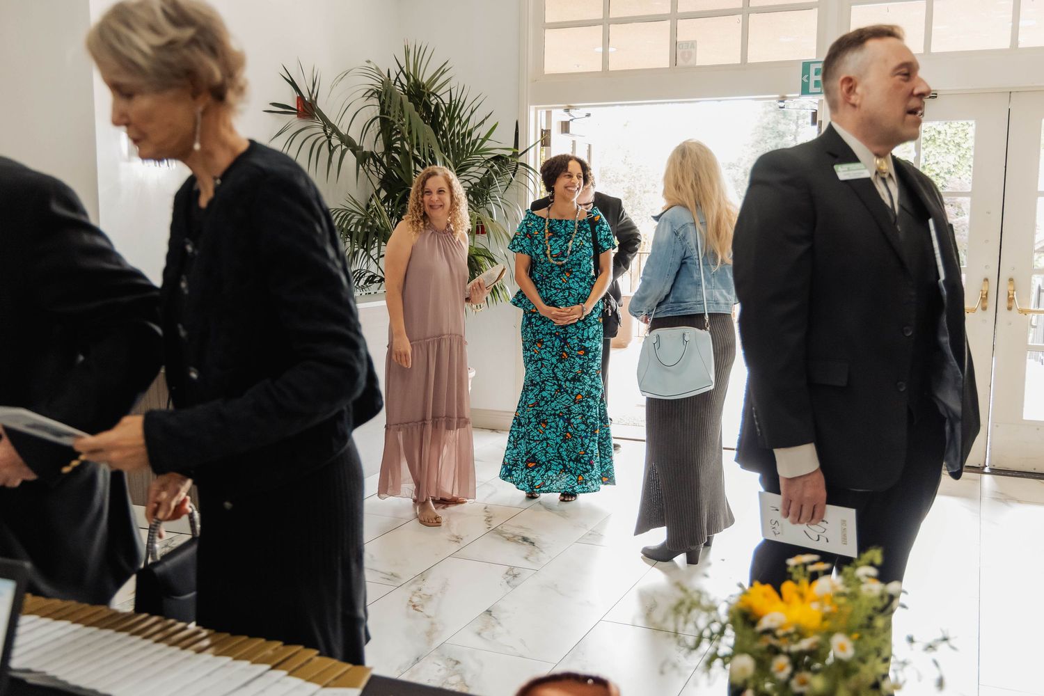 Elegantly dressed guests mingle in a bright marble foyer during a formal event or wedding reception.
