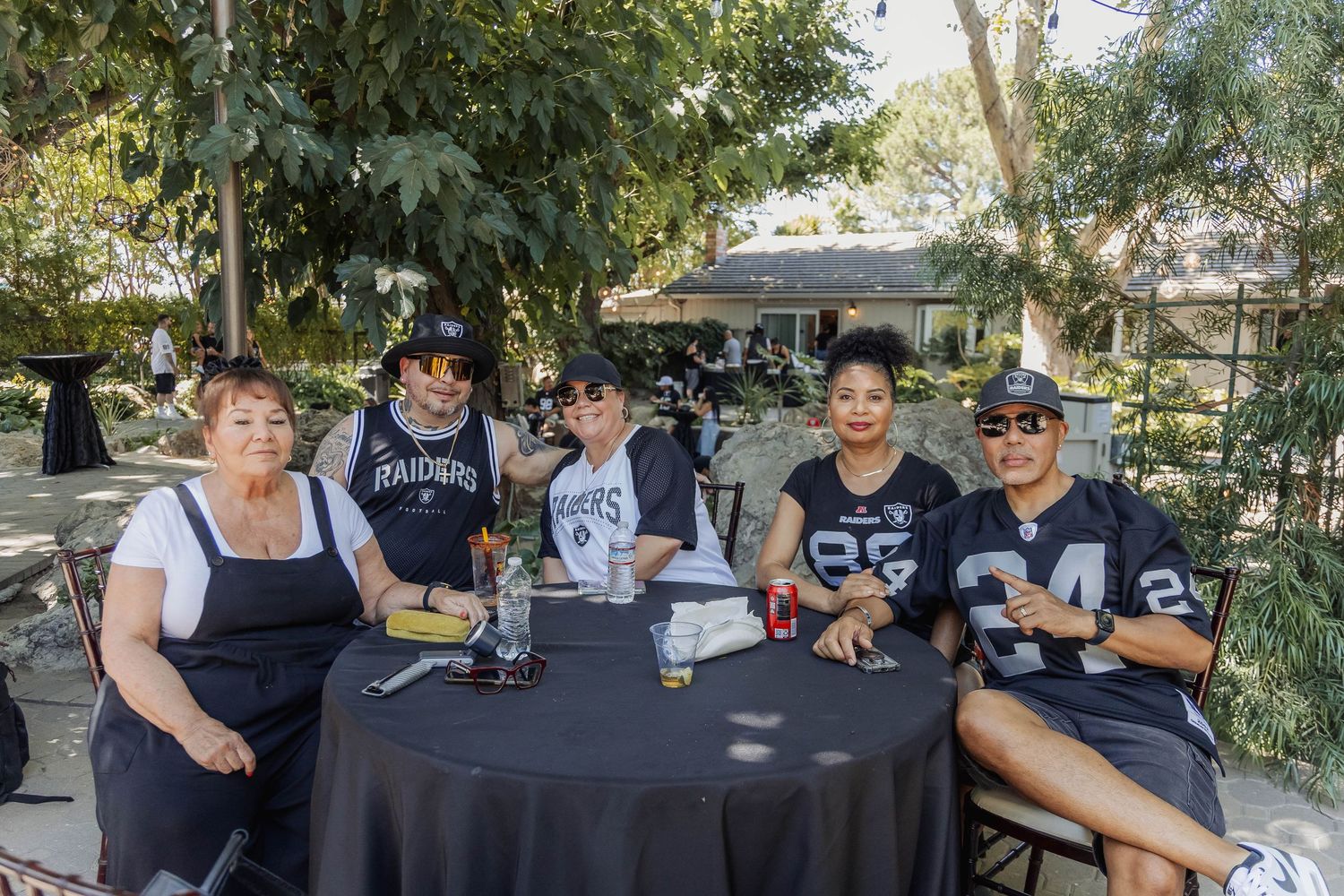 Five Raiders fans smiling together at round table during outdoor NFL themed fan gathering.