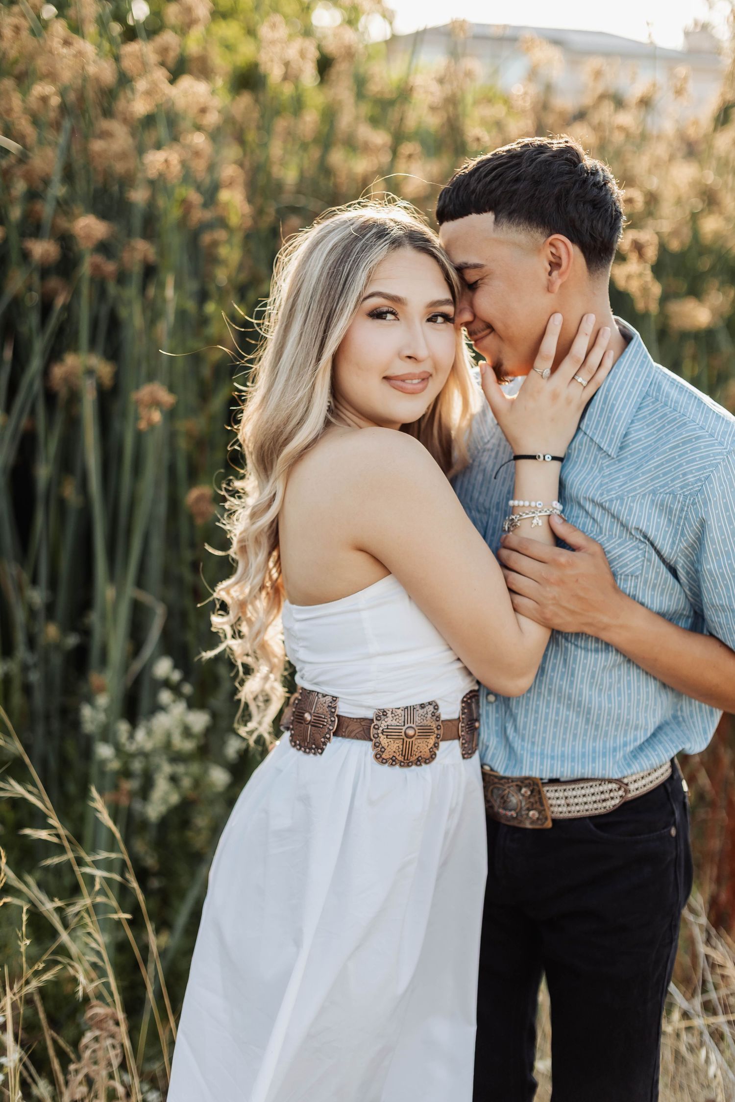 Romantic couple in western attire embracing during golden hour photoshoot with decorative belt detail.