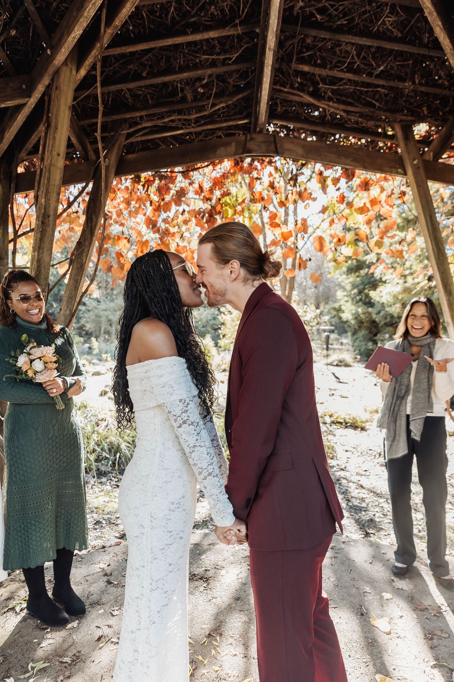 Wedding ceremony under wooden gazebo with autumn foliage in background.