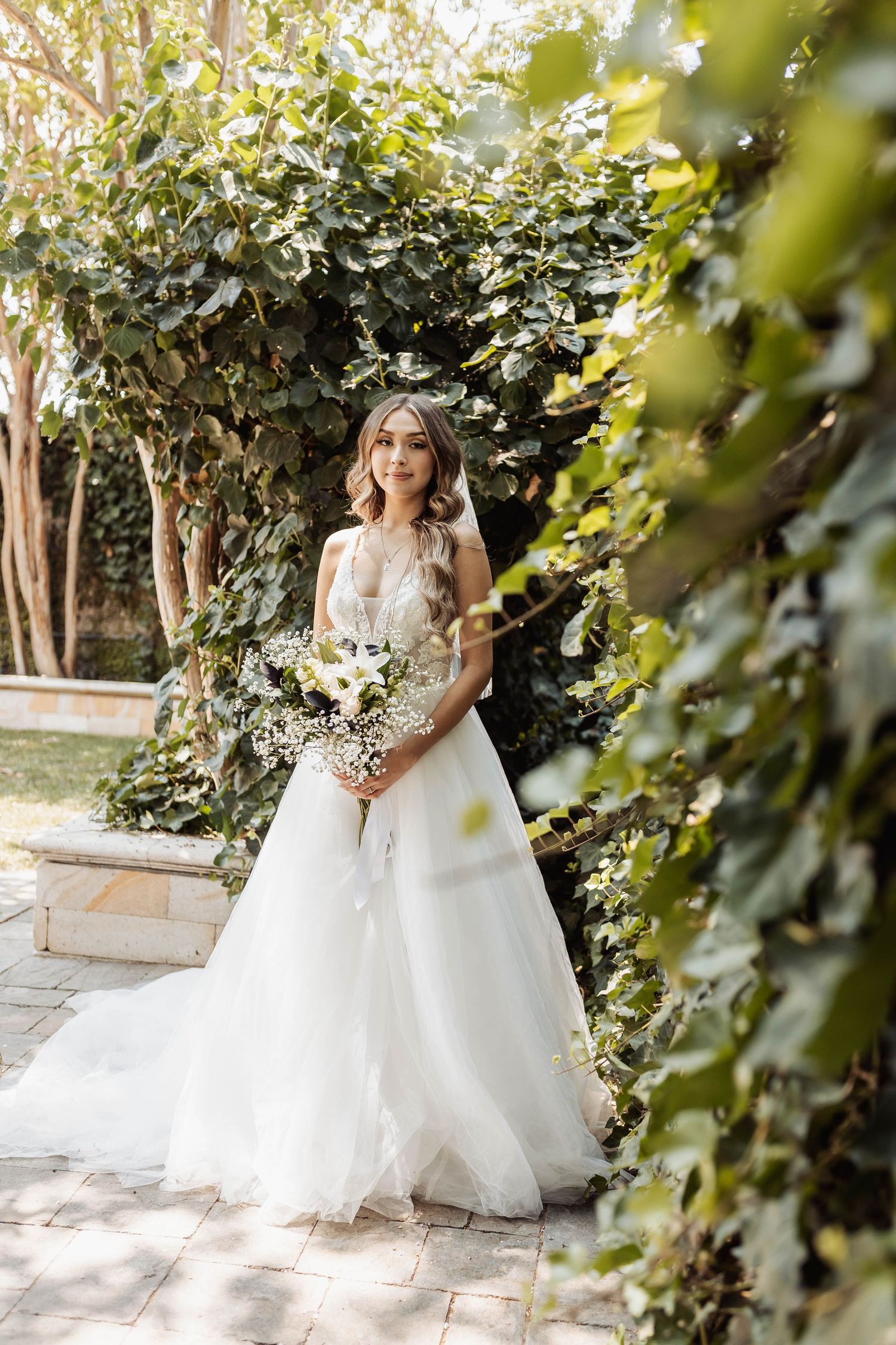A dreamy bridal portrait amid garden foliage with soft natural lighting and a full tulle wedding gown.