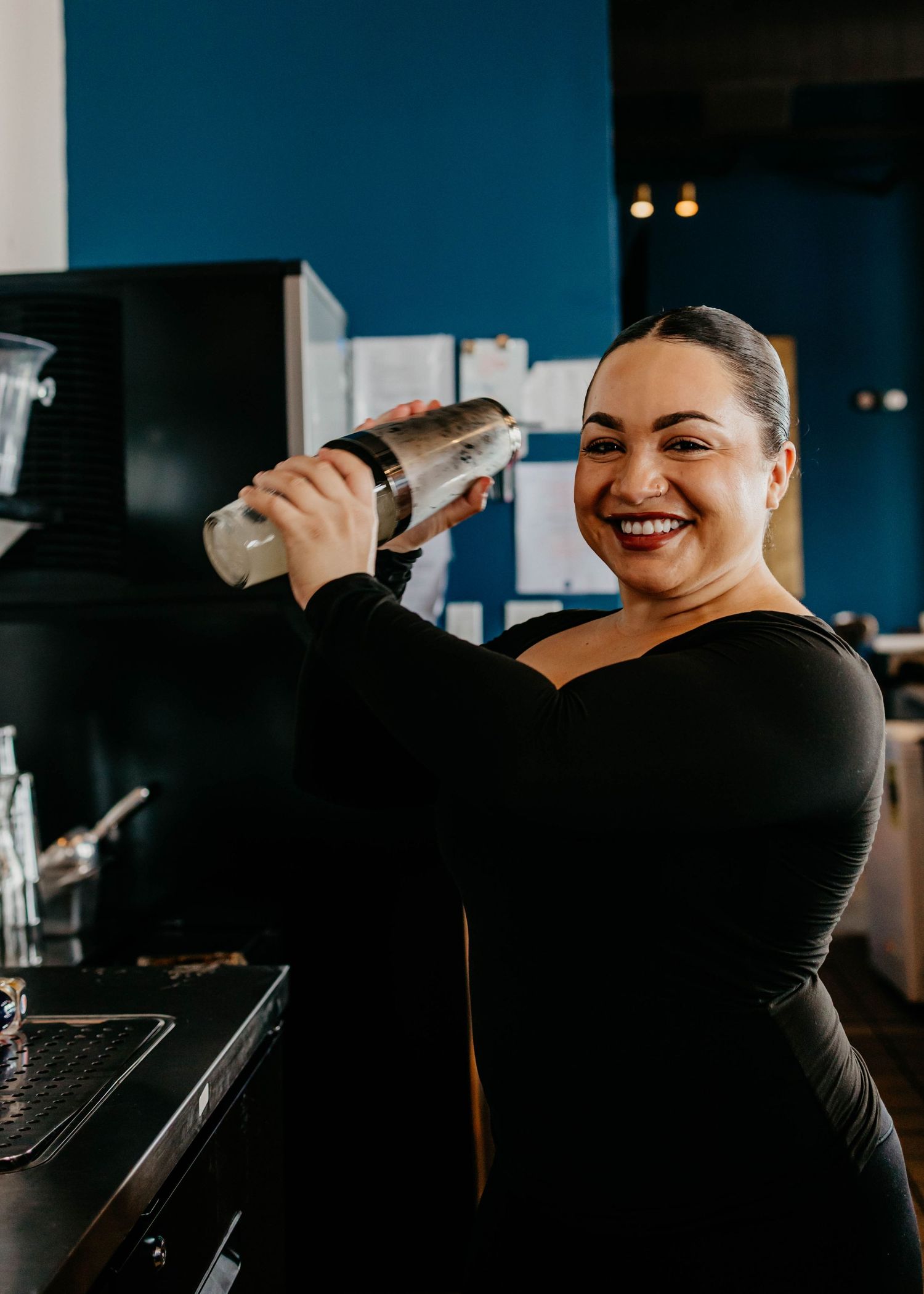 Staff member in black preparing drinks behind bar counter.