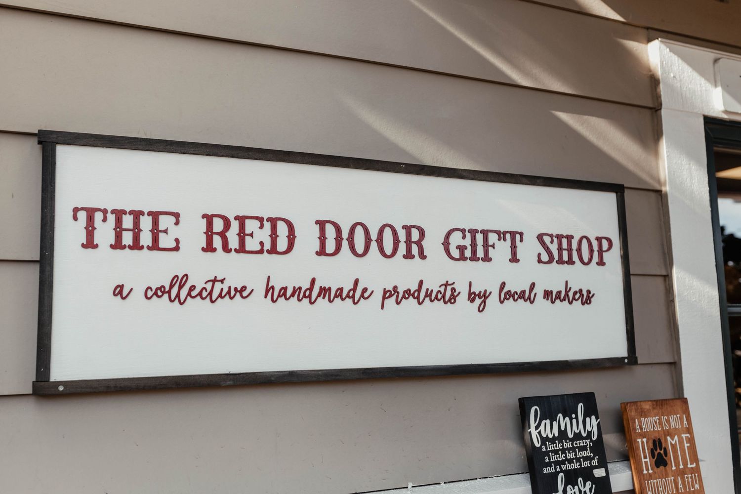 Red and white storefront sign reading 'The Red Door Gift Shop' mounted on exterior wall.