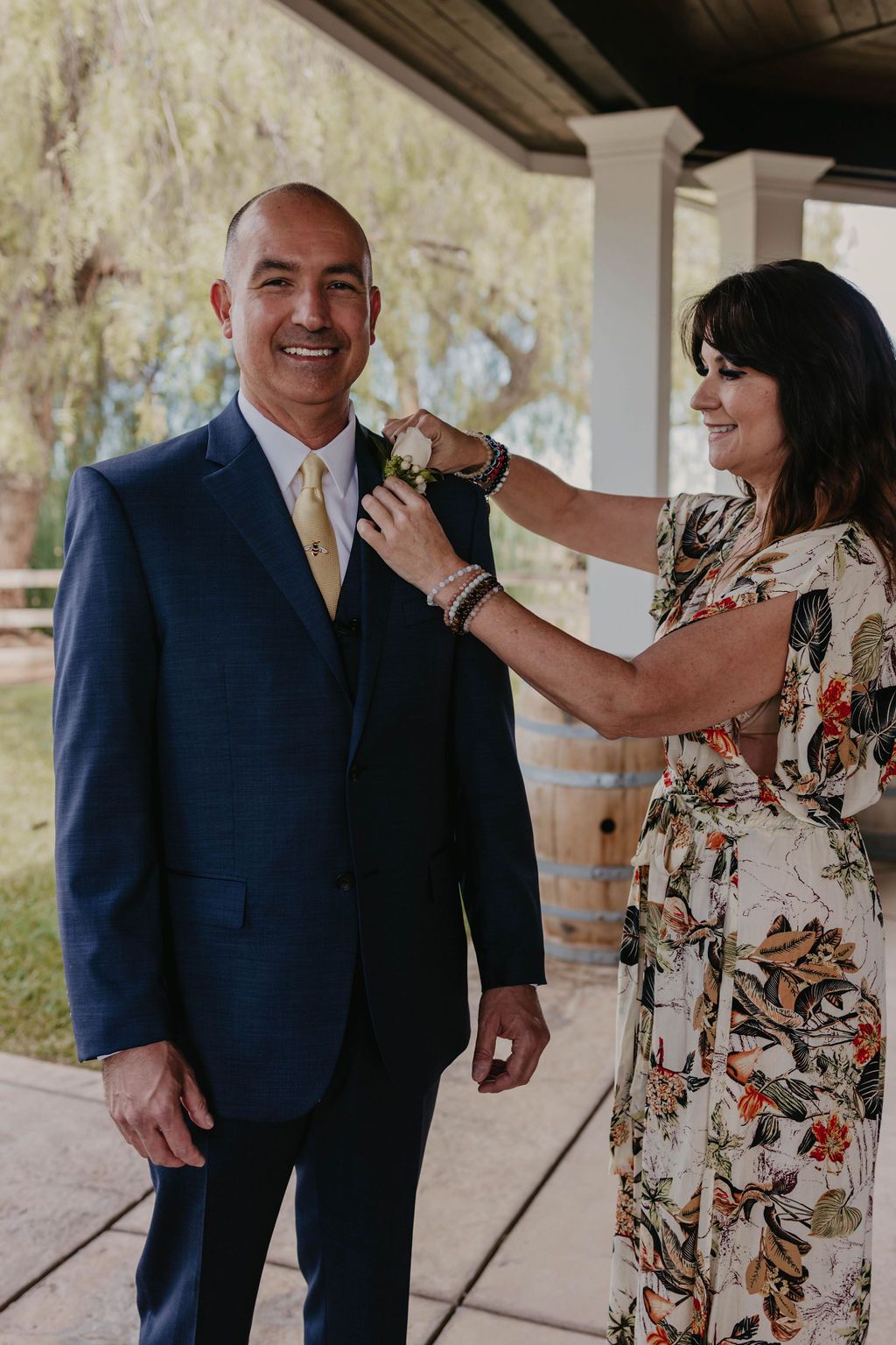 Someone adjusts a tie on a person wearing a navy suit during wedding preparations.