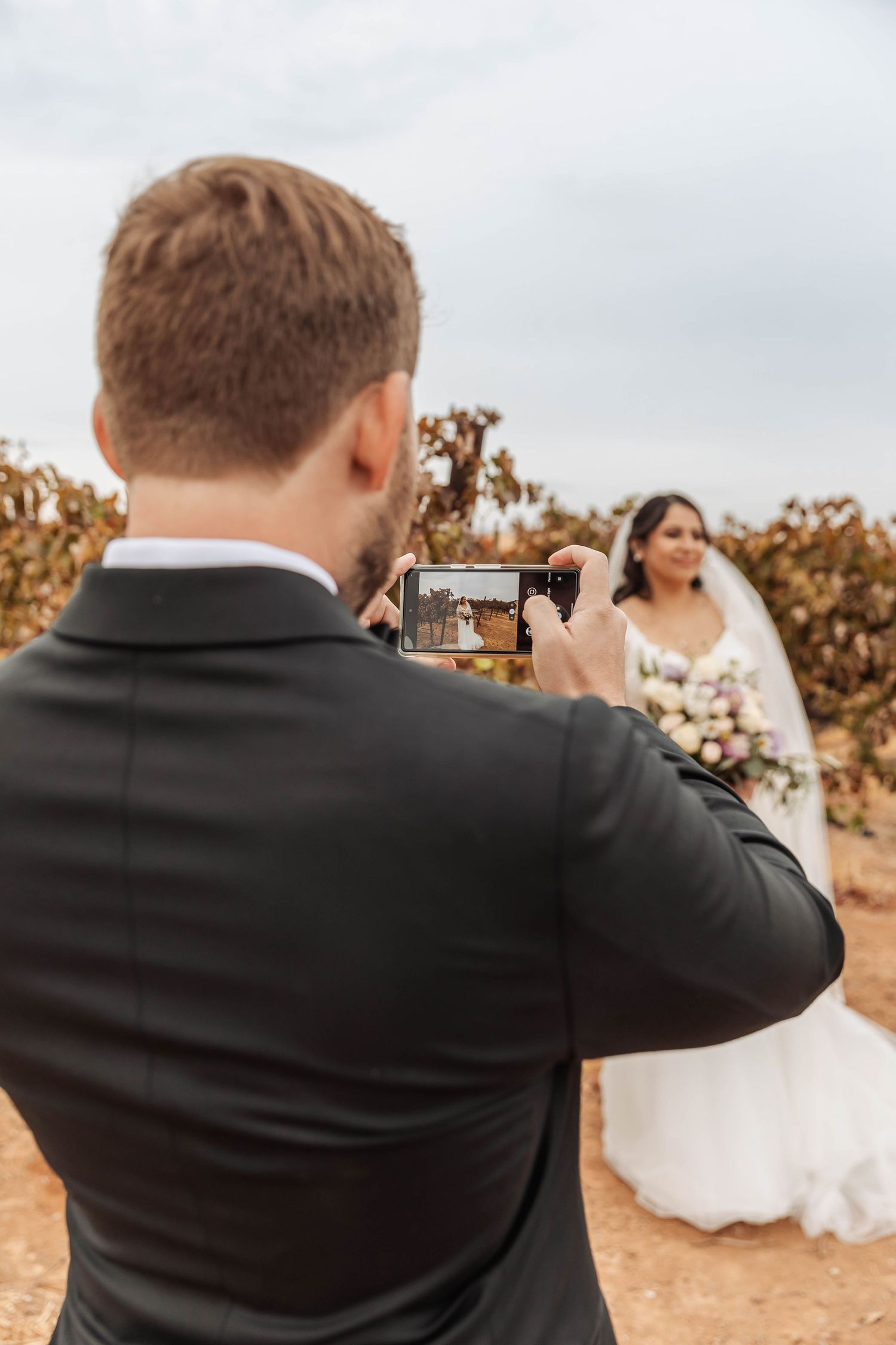 Wedding photographer captures bride and groom in a vineyard setting.