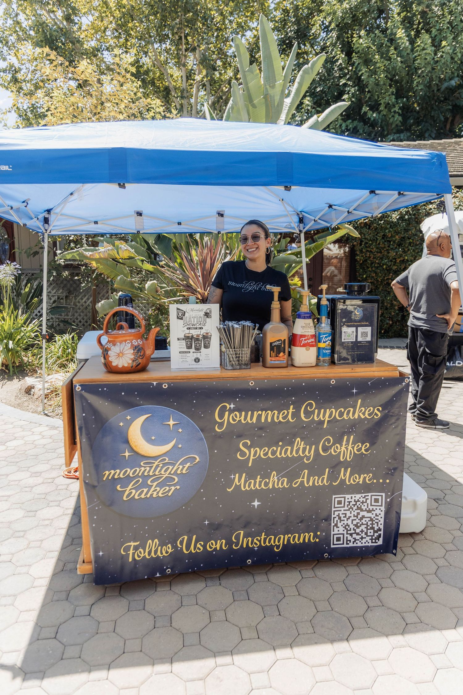 Moonlight Baker vendor booth offering gourmet cupcakes specialty coffee and matcha at outdoor market.
