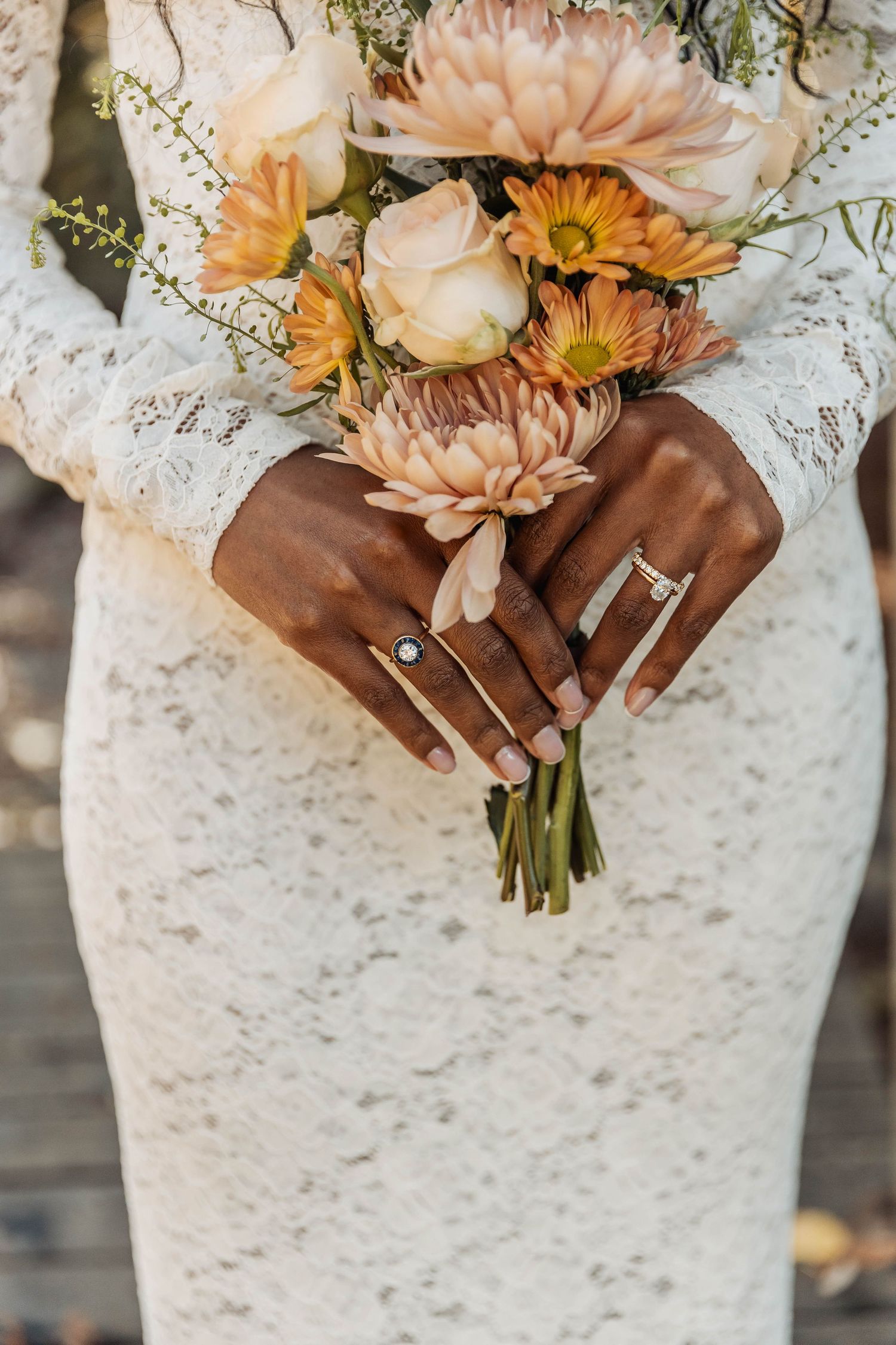Bridal bouquet of peach dahlias and roses held against white lace dress.