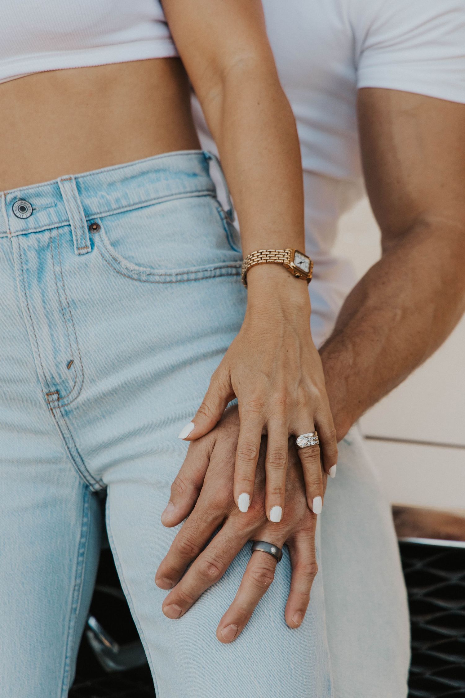 Close-up shots of hands wearing engagement rings against light denim.