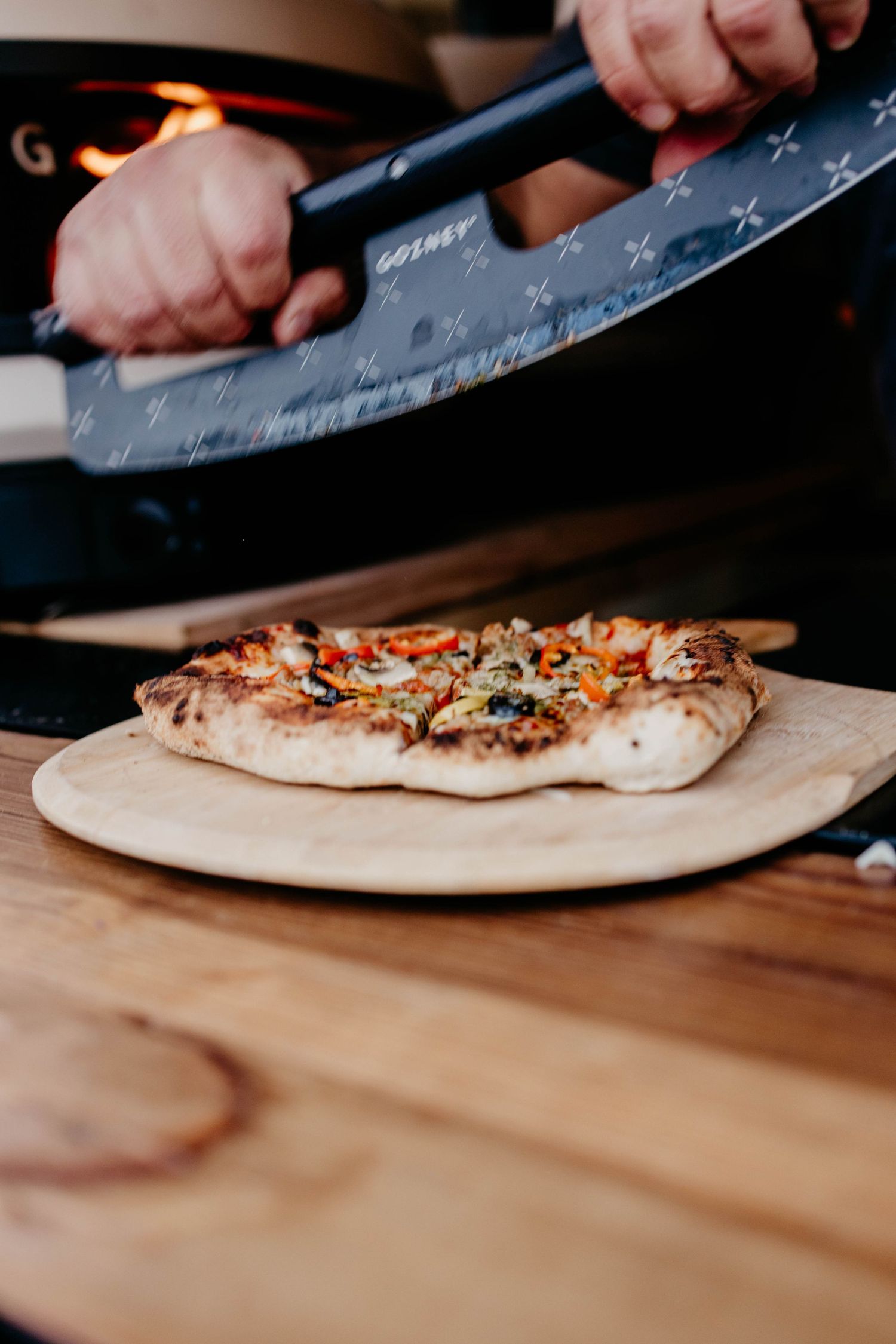 Pizza being sliced on a wooden cutting board with a large knife.