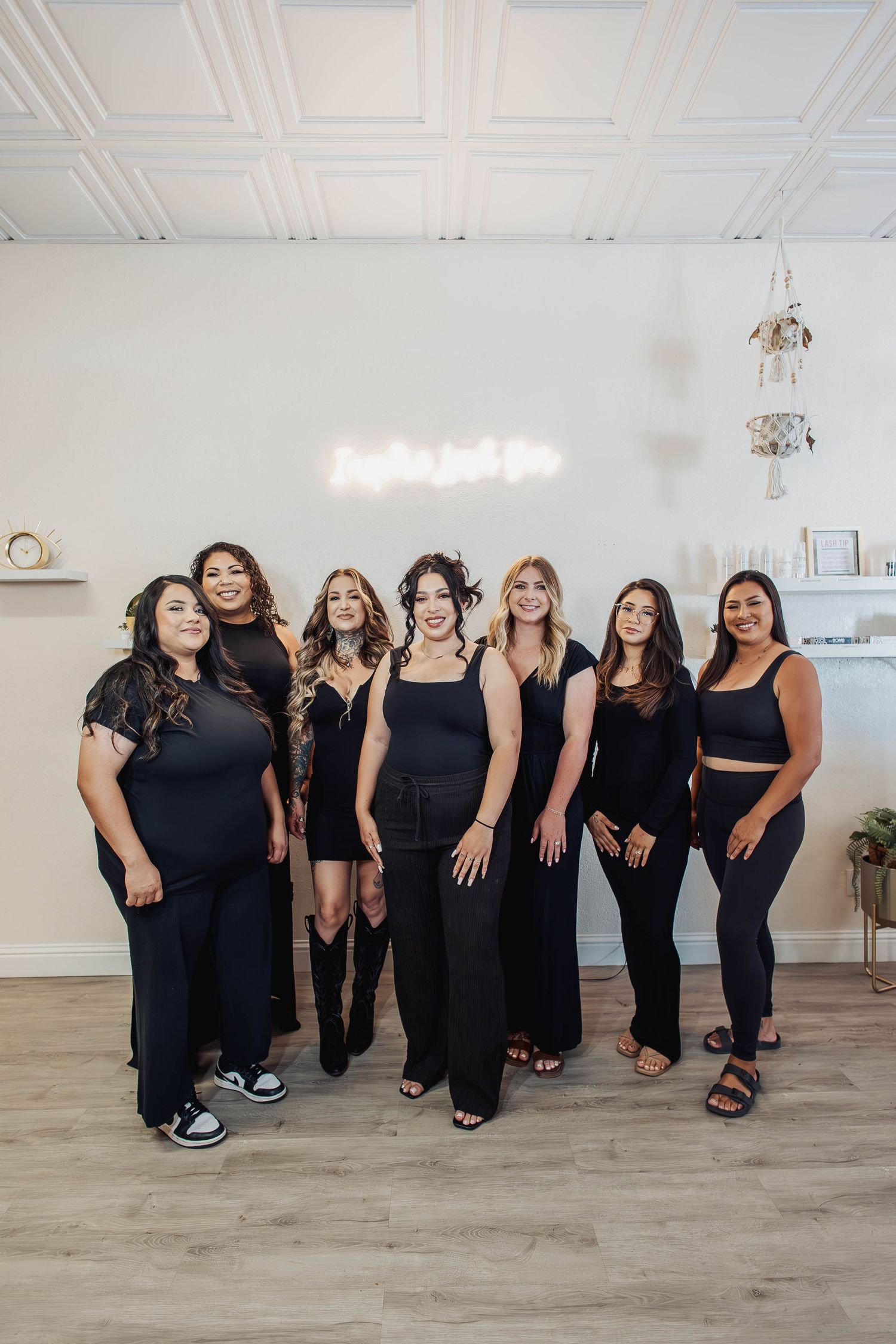 Group portrait of team members in matching black outfits posing together on light wooden flooring.