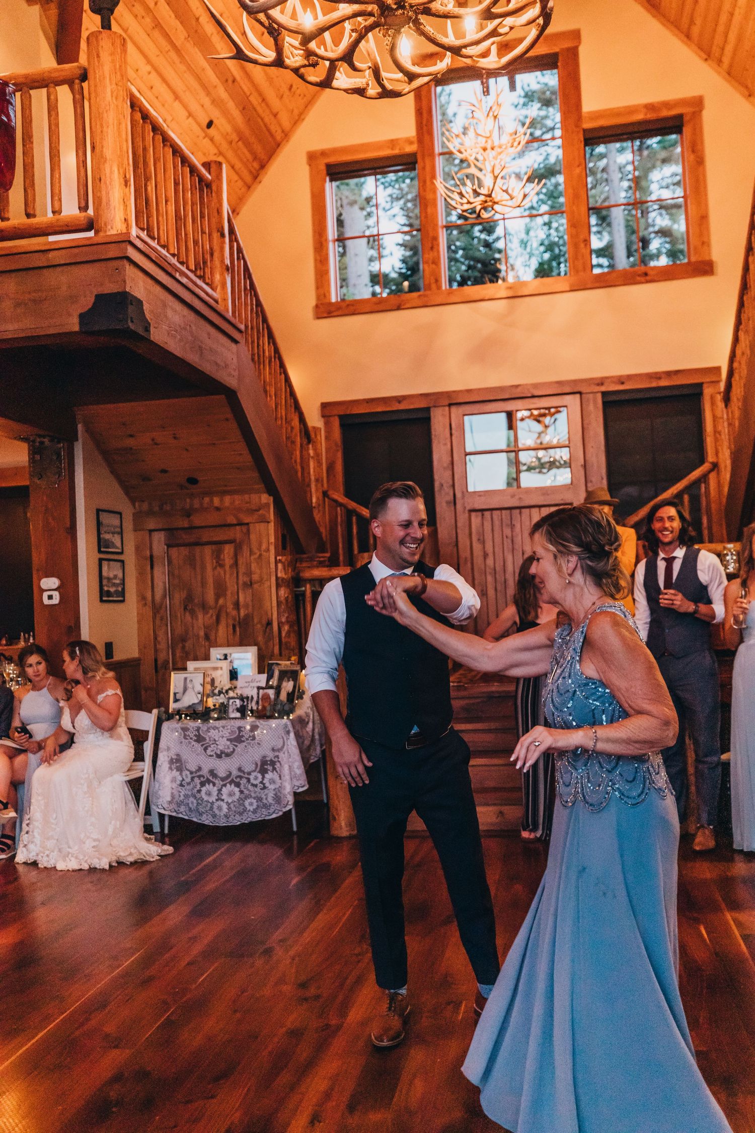 Couple dancing together at a rustic wedding reception venue with wooden floors and high vaulted ceilings.