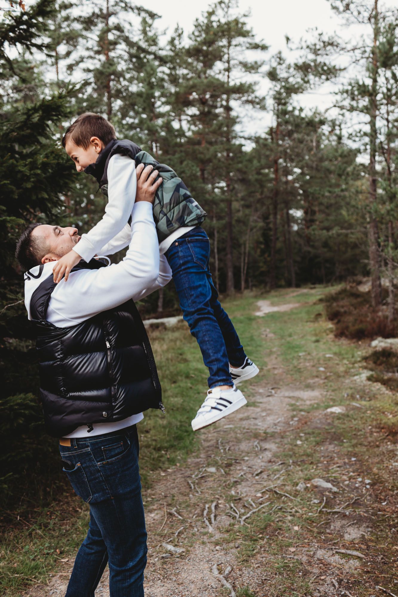 Playful moment captured as someone lifts a child high in the air on a forest path.