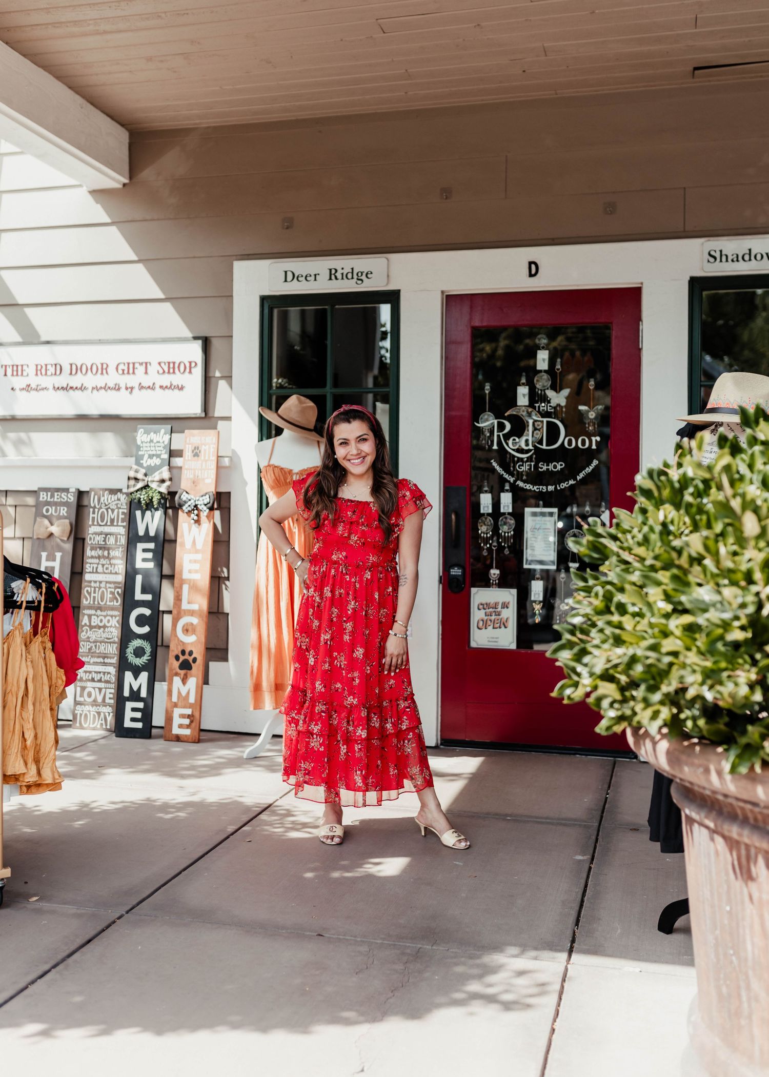 Storefront of a boutique with red door and welcome sign under a covered walkway.