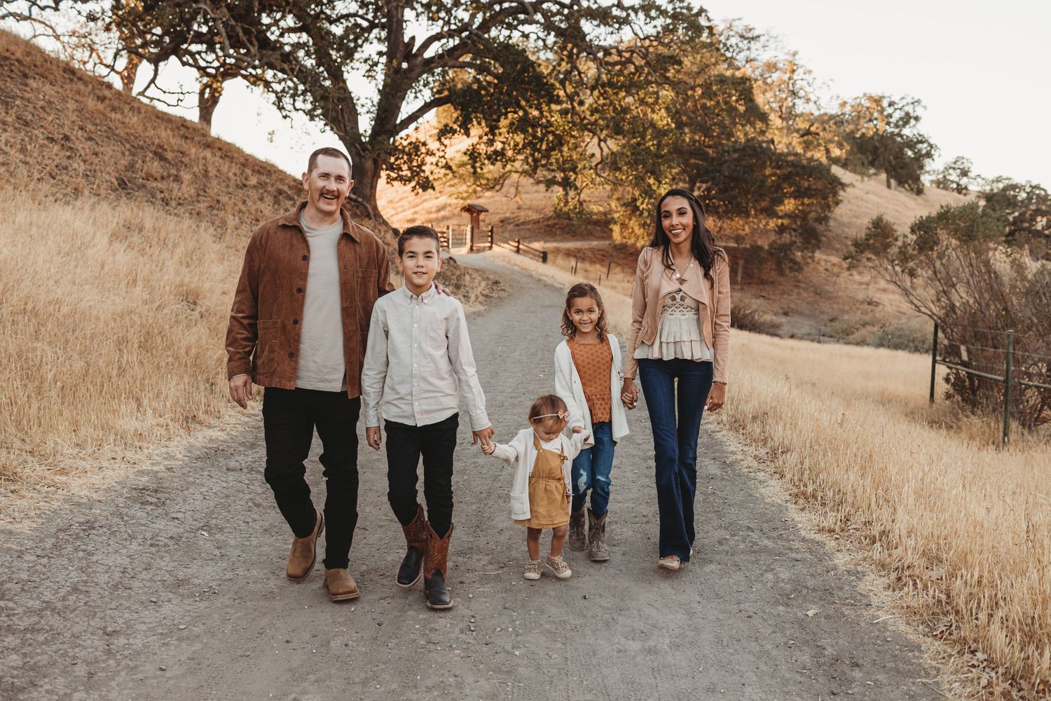 Family walking together on dusty trail during golden hour with dry grass in background.