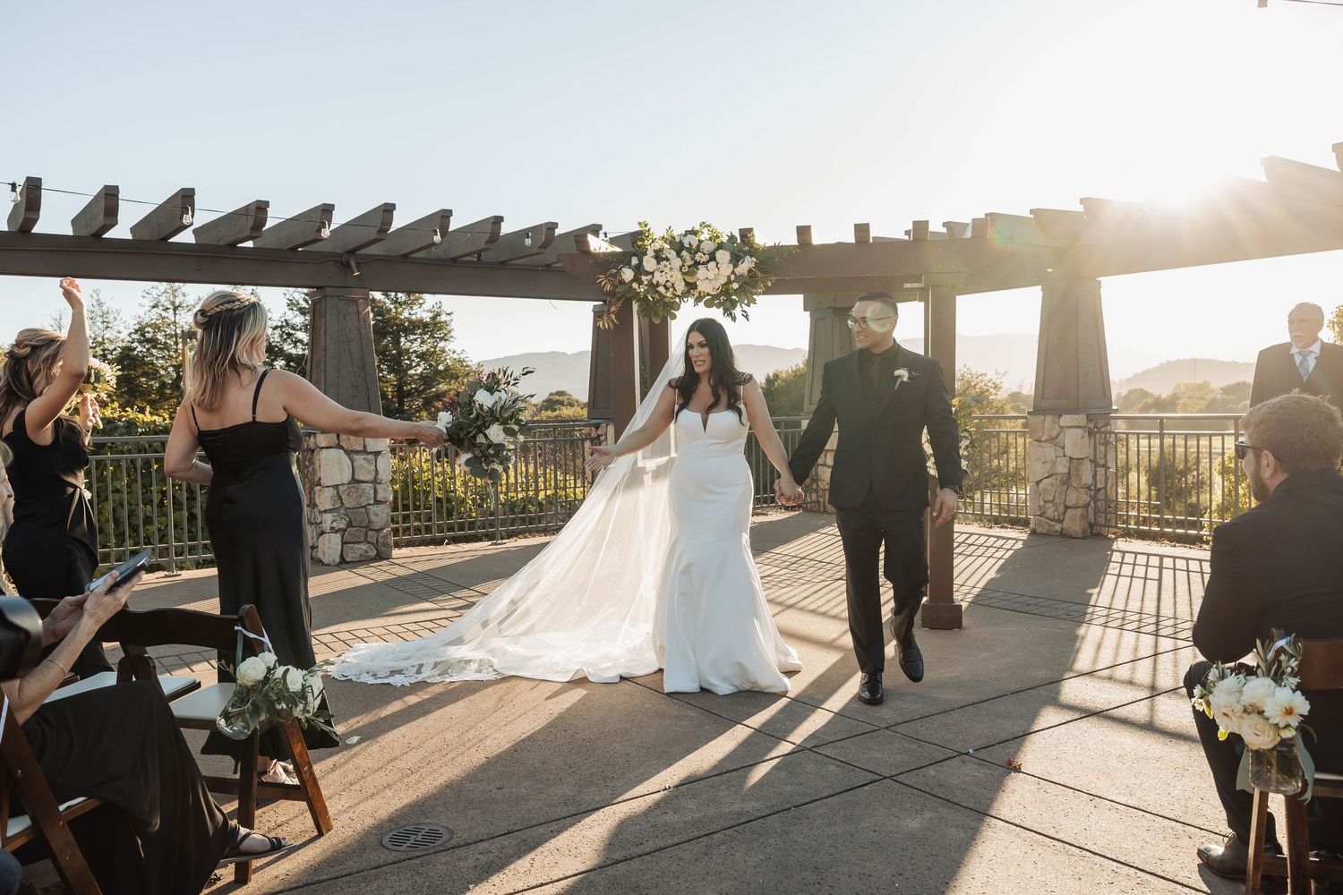 Wedding ceremony setup at sunset with pergola and guests gathered outdoors.