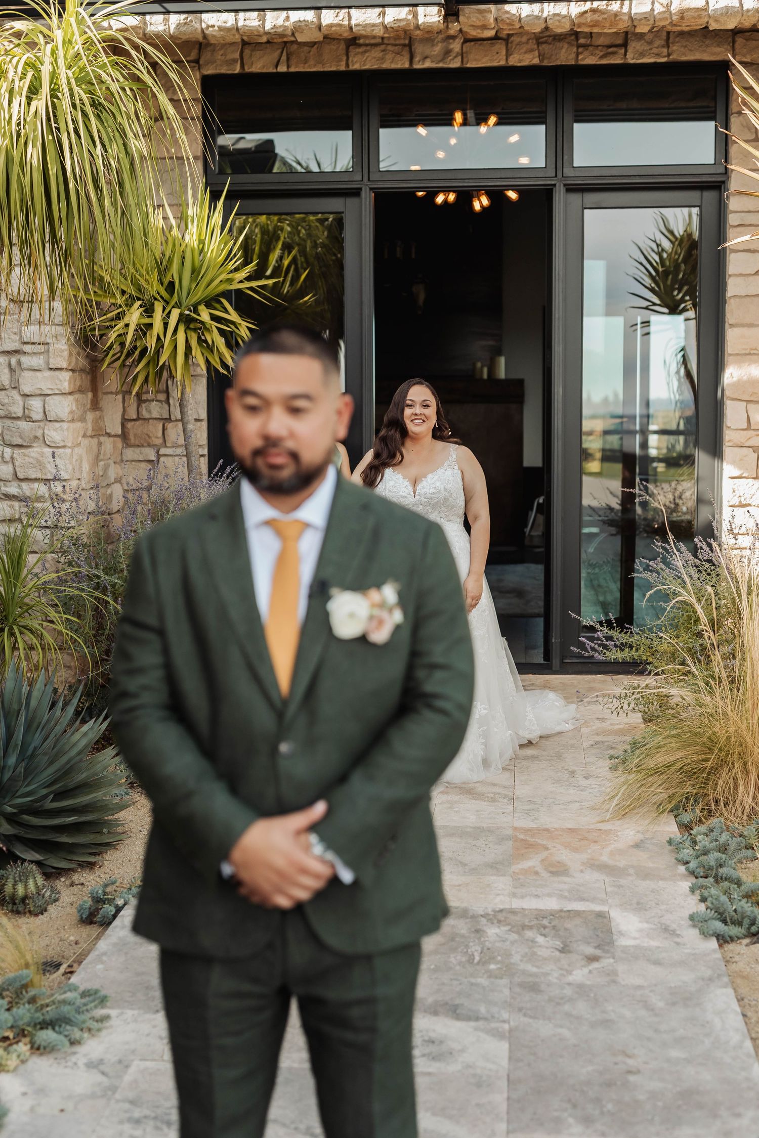 First look moment at modern venue with stone walls and tropical plants.