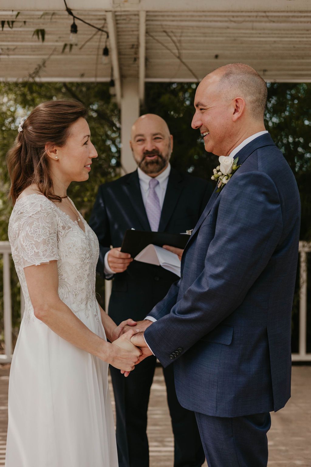An outdoor wedding ceremony with couple holding hands while exchanging vows under covered porch.