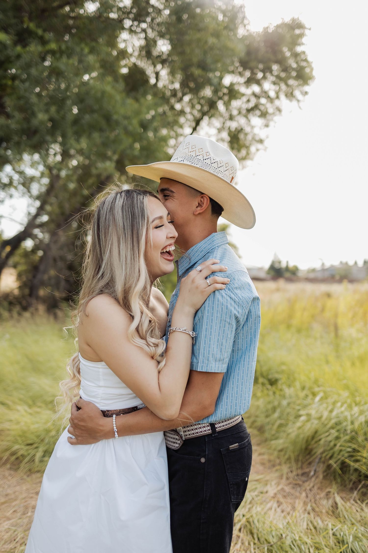 Romantic couple embracing in a sunlit field with cowboy hat.
