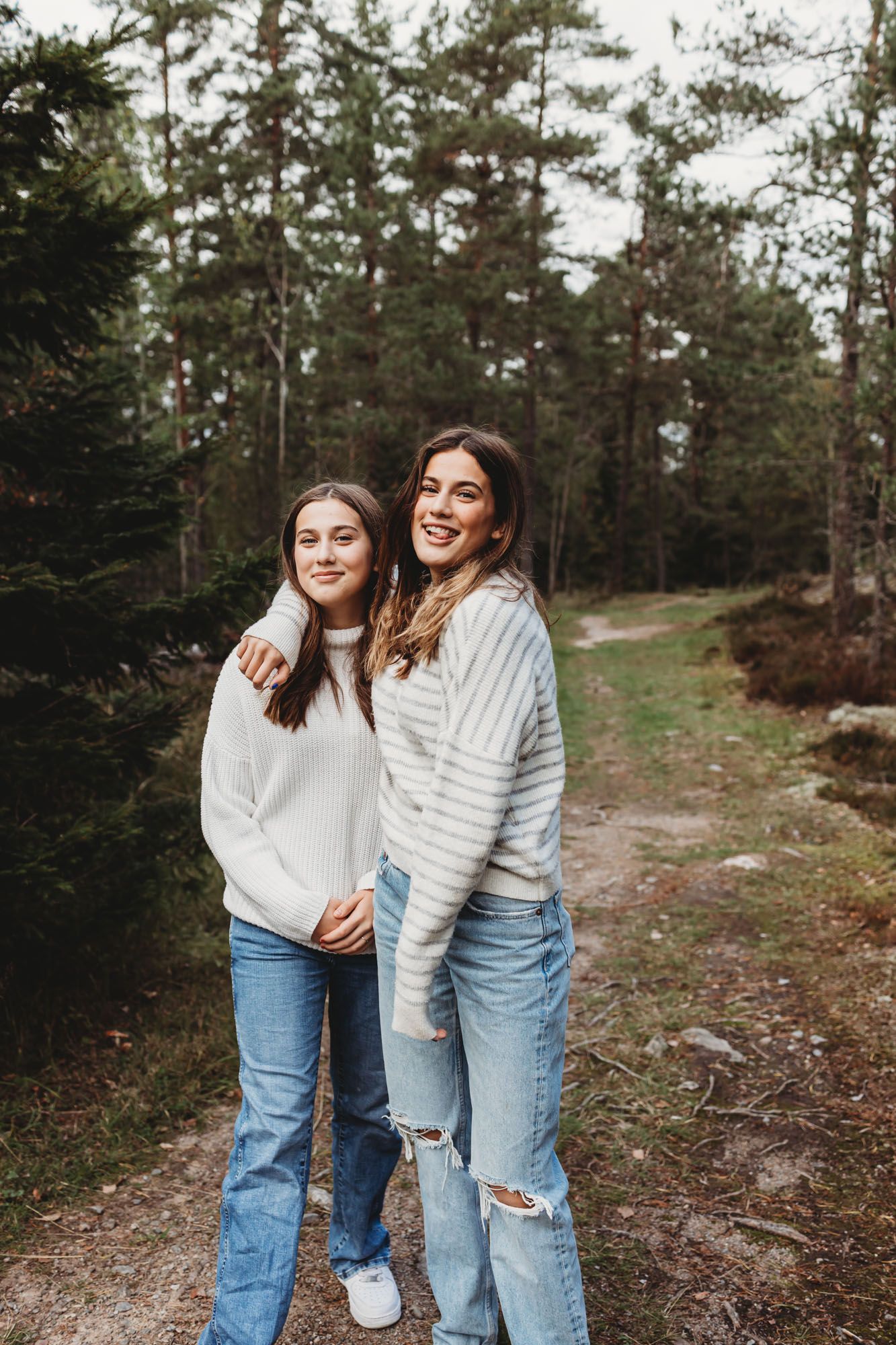 Friends in matching jeans and sweaters pose together on a forest path.
