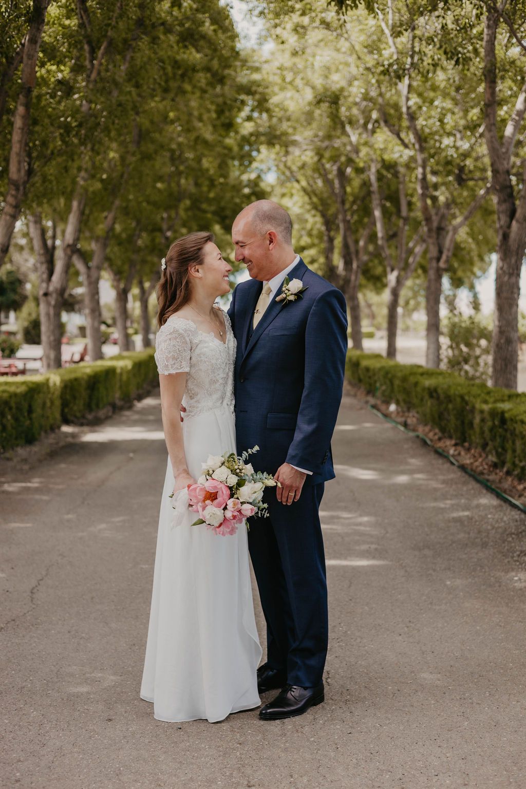 Candid moment between newlyweds on tree-lined pathway during wedding portraits.