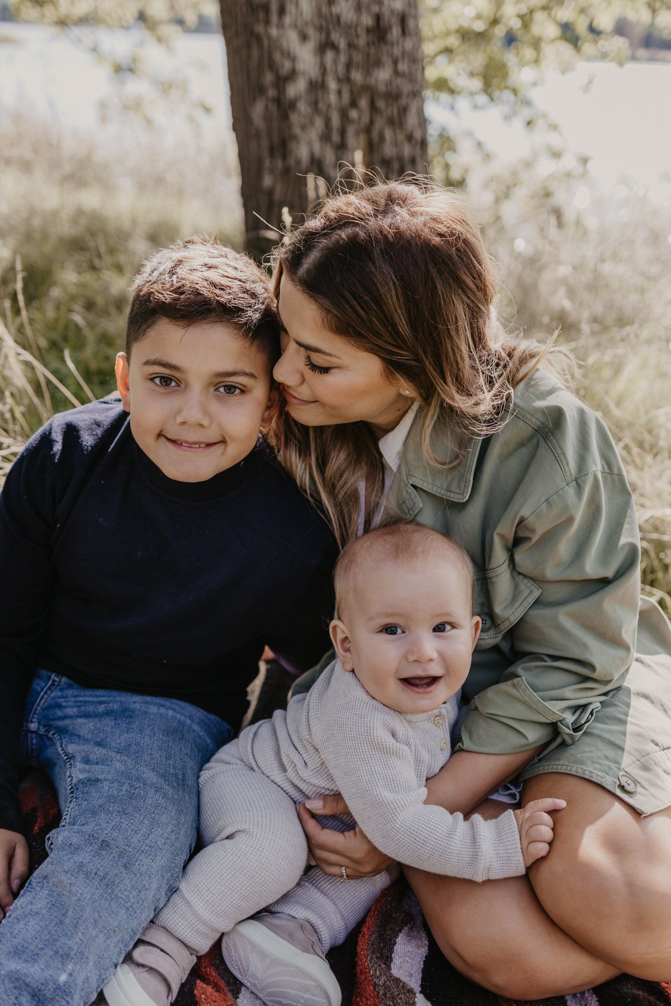 Tender family moment captured outdoors with siblings and parent on picnic blanket.