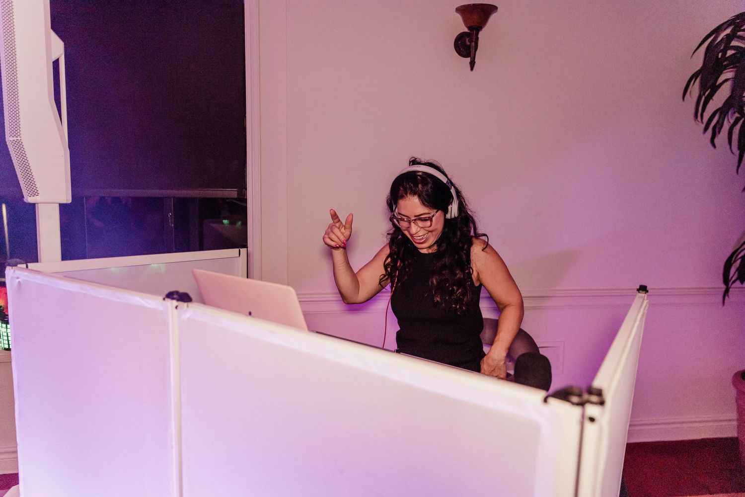 A DJ performs enthusiastically behind a white booth at a nighttime event.