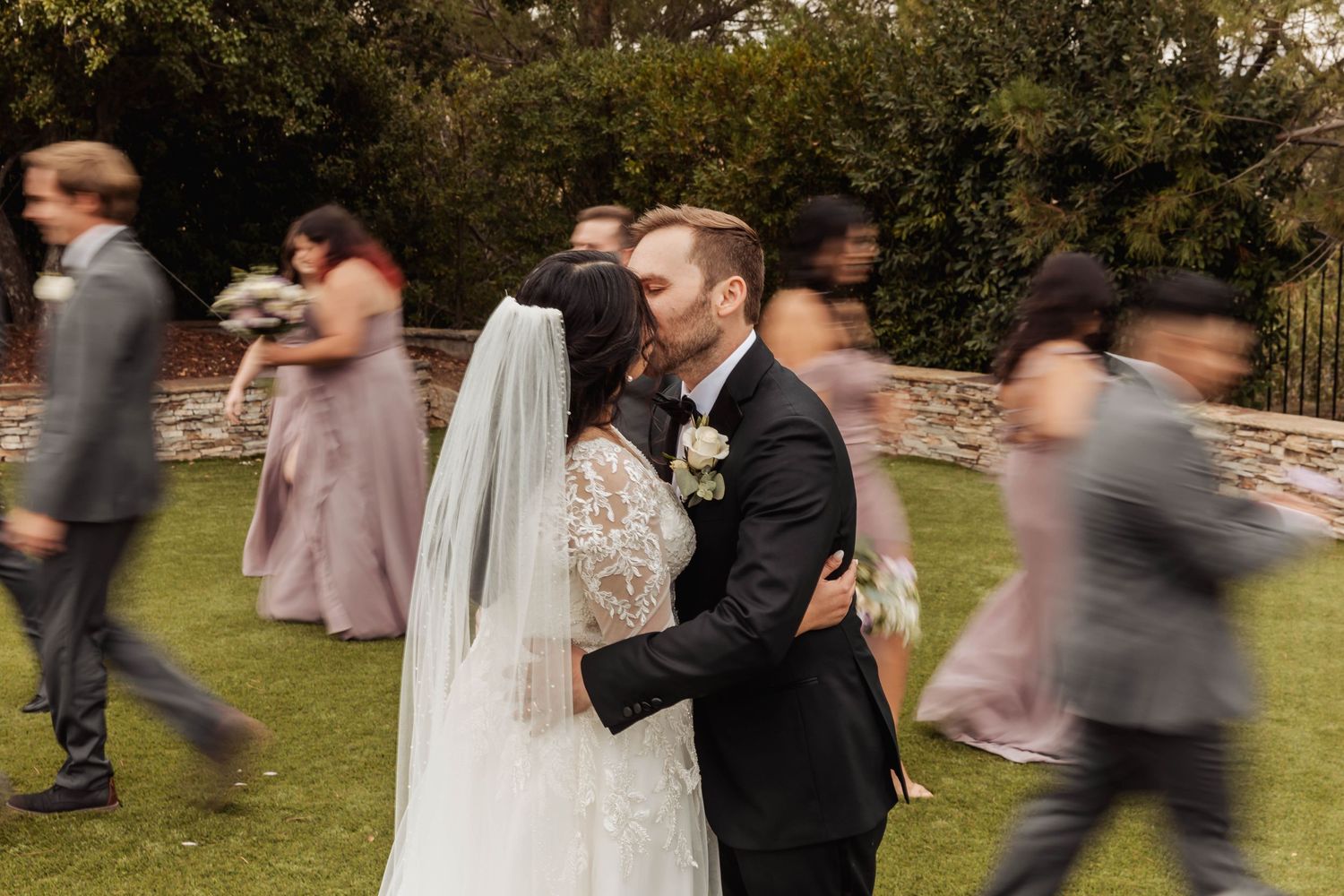 Wedding ceremony guests gathered outdoors in a garden setting with soft pink and natural tones.
