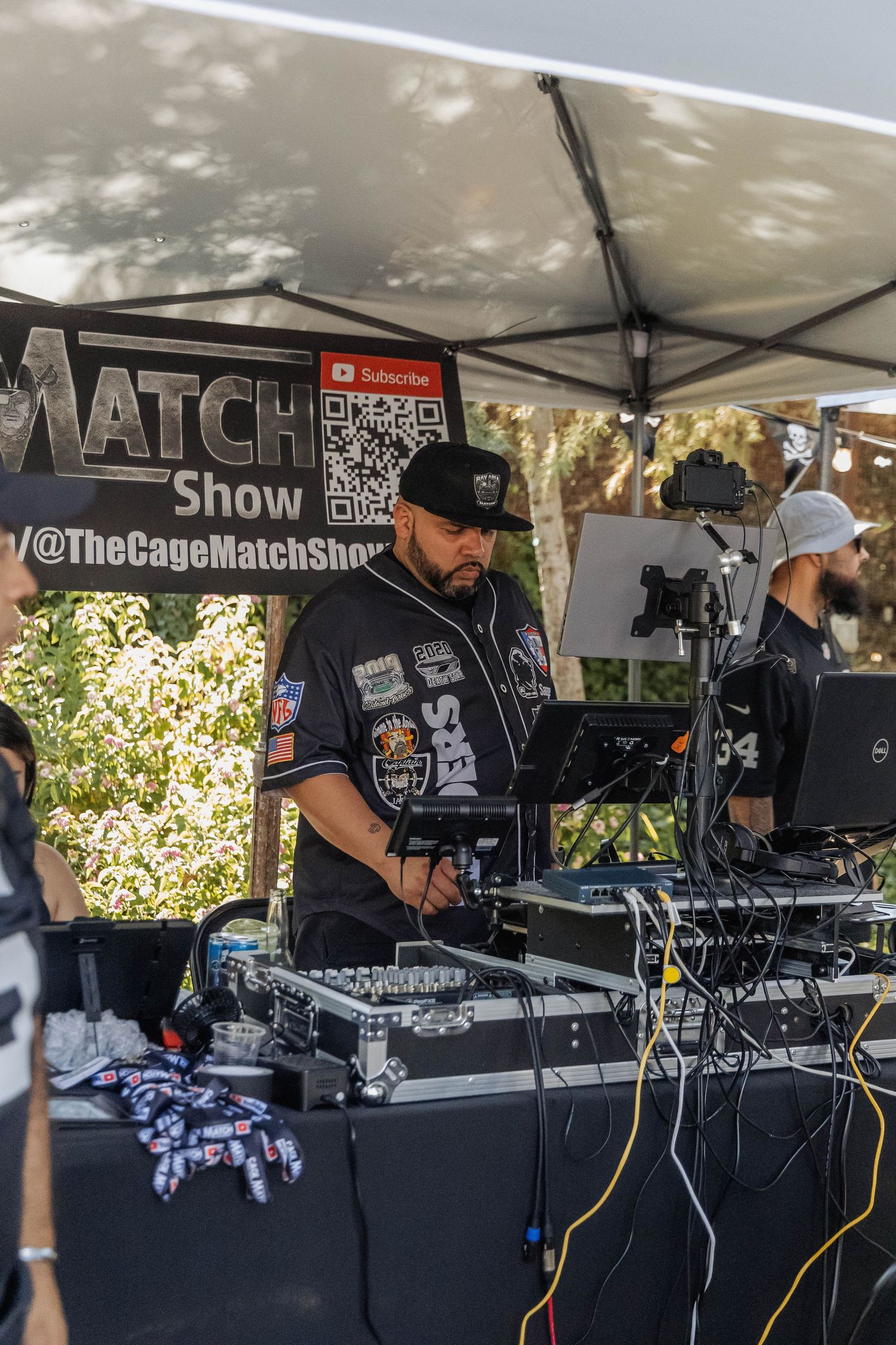DJ operates mixing equipment at The Cage Match Show outdoor event booth.