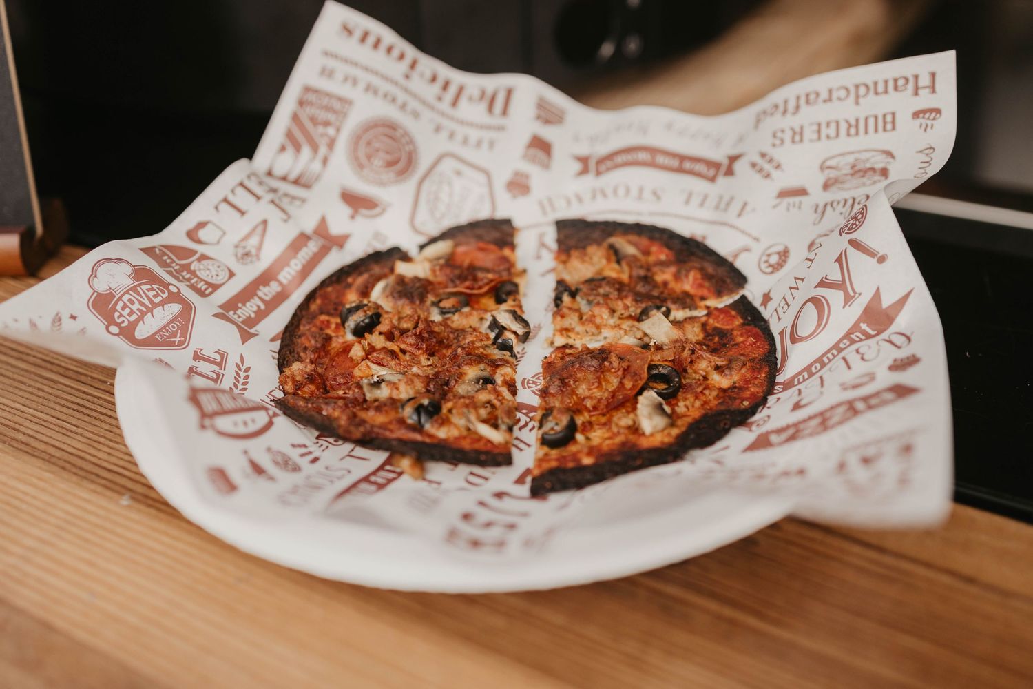 Fresh baked pizzas in branded paper wrapping on a wooden surface.