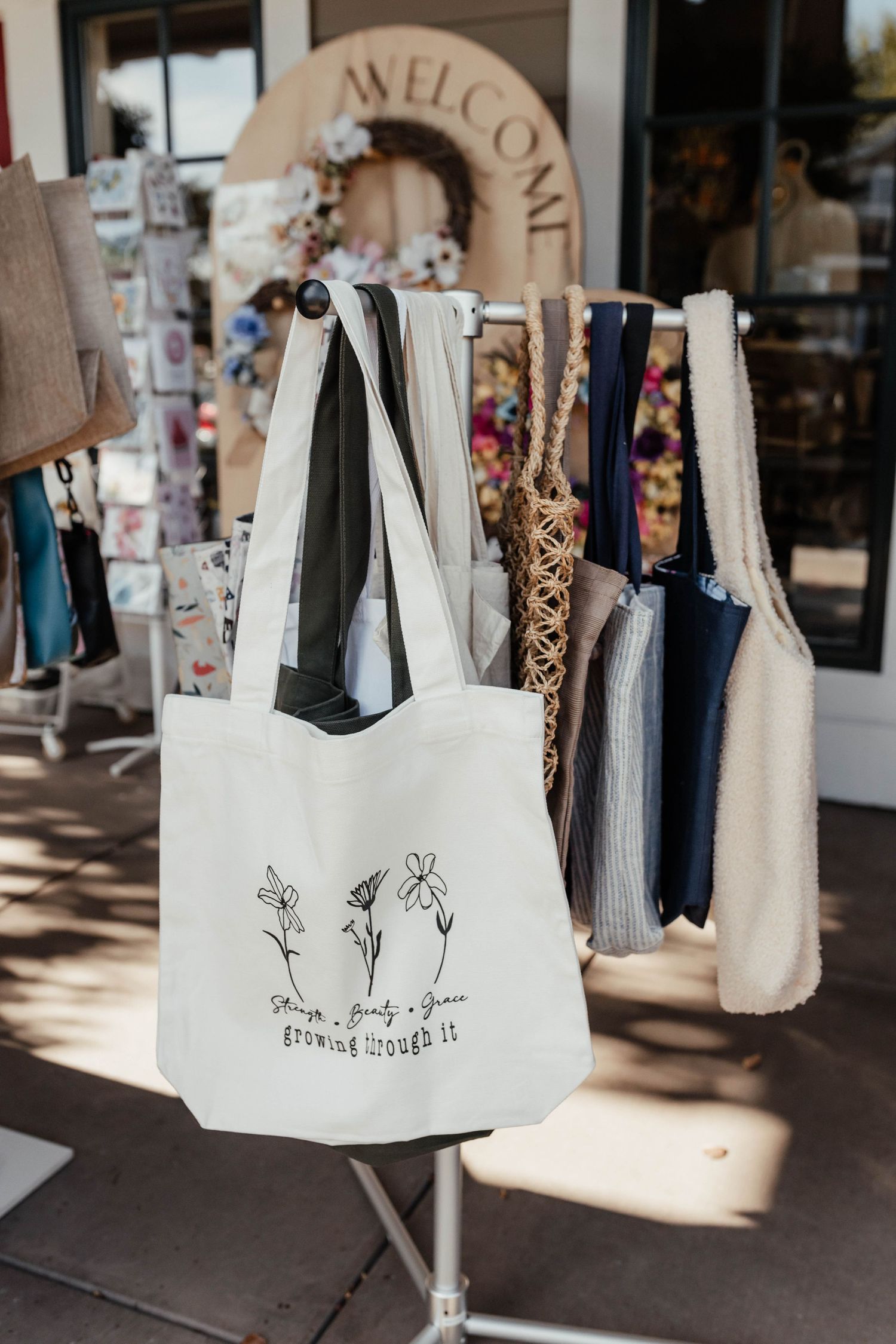 Canvas tote bags with floral designs hanging on display outside a retail store.