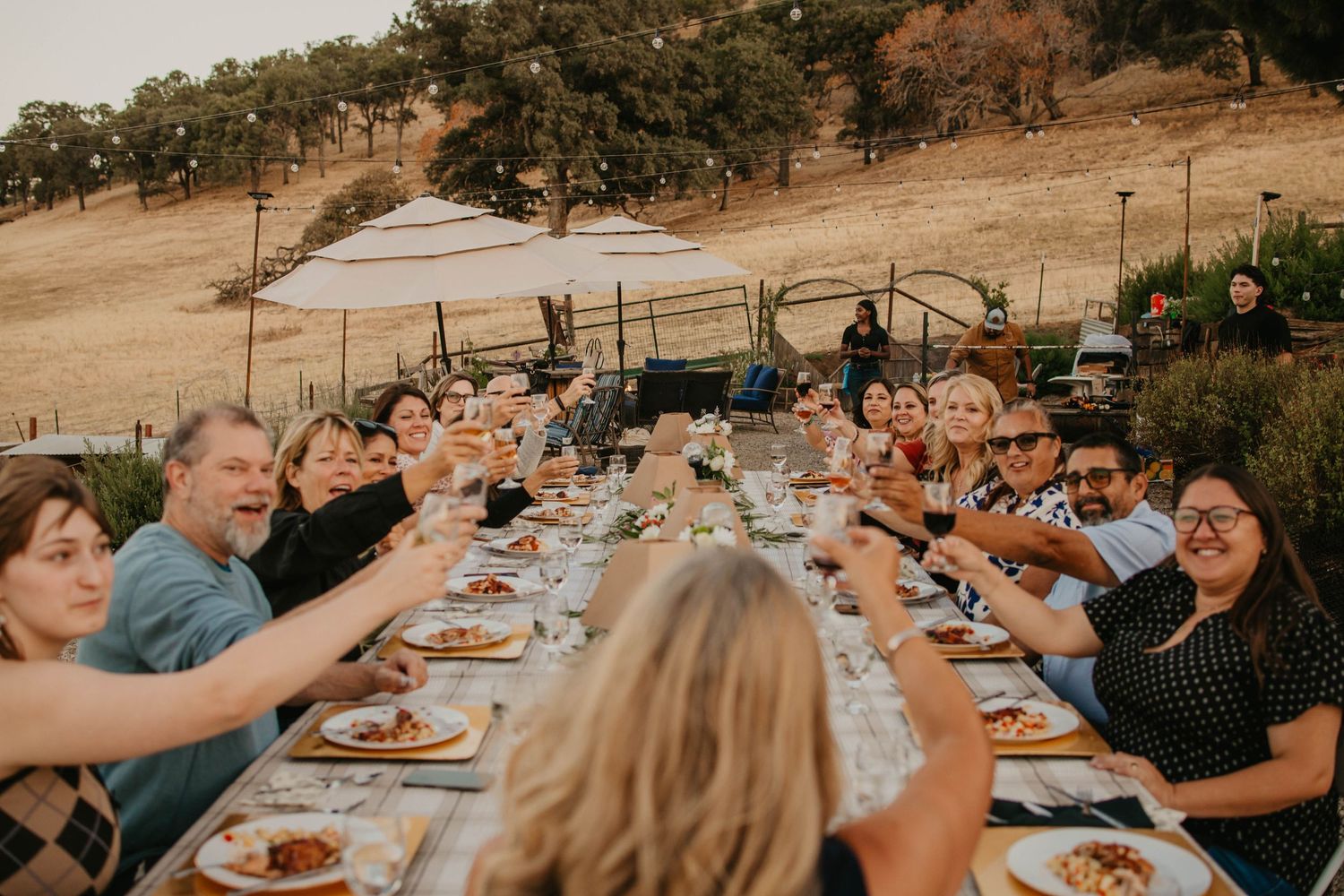 A group enjoying a festive outdoor dining experience at a long table in a rustic setting.