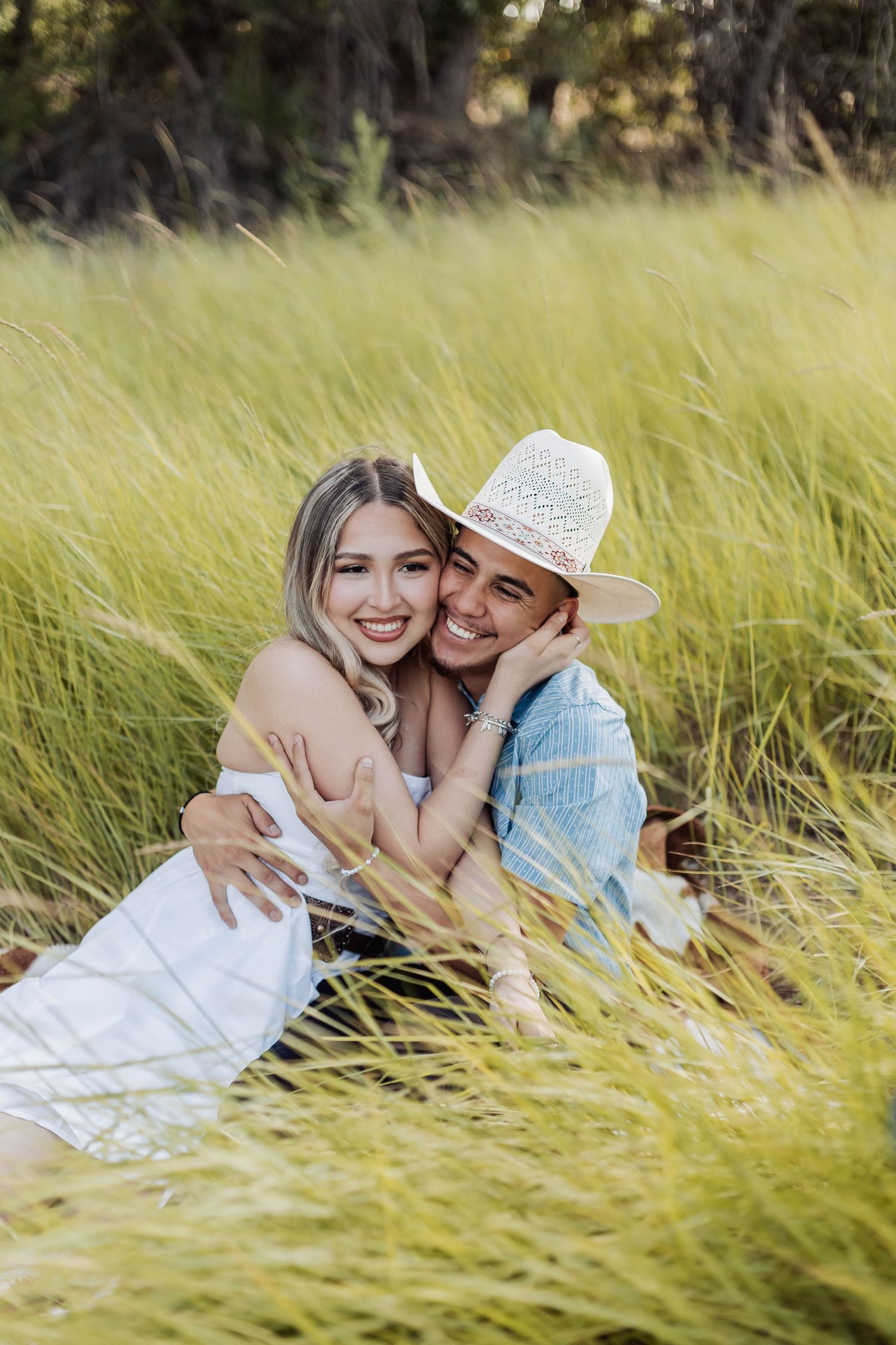 Happy couple lying in tall grass field wearing western inspired outfits.