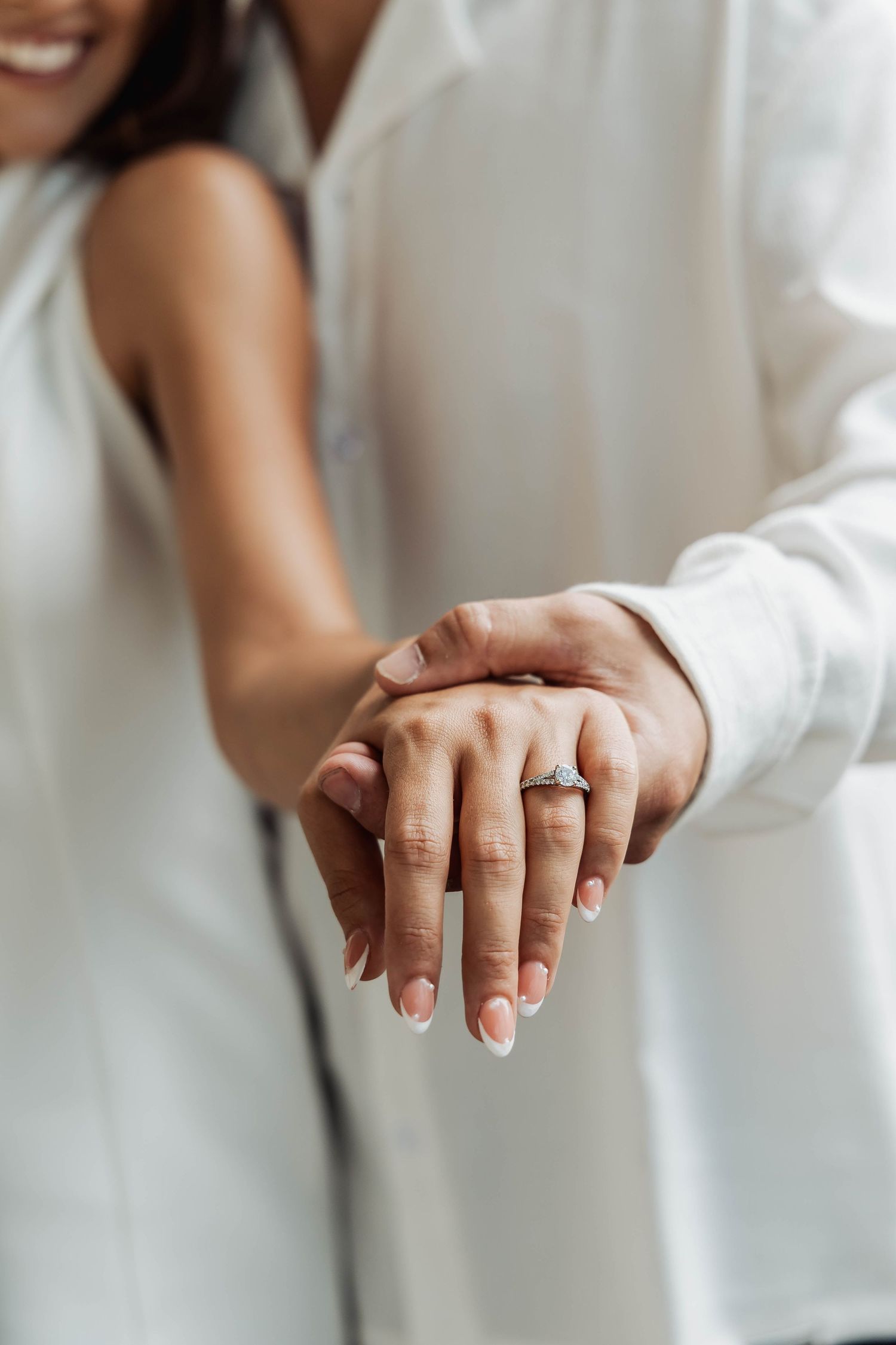 Close-up of hands showing engagement ring against white clothing.