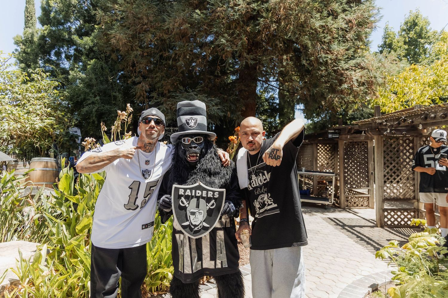 Three men in Las Vegas Raiders NFL fan gear posing together at outdoor tailgate party.