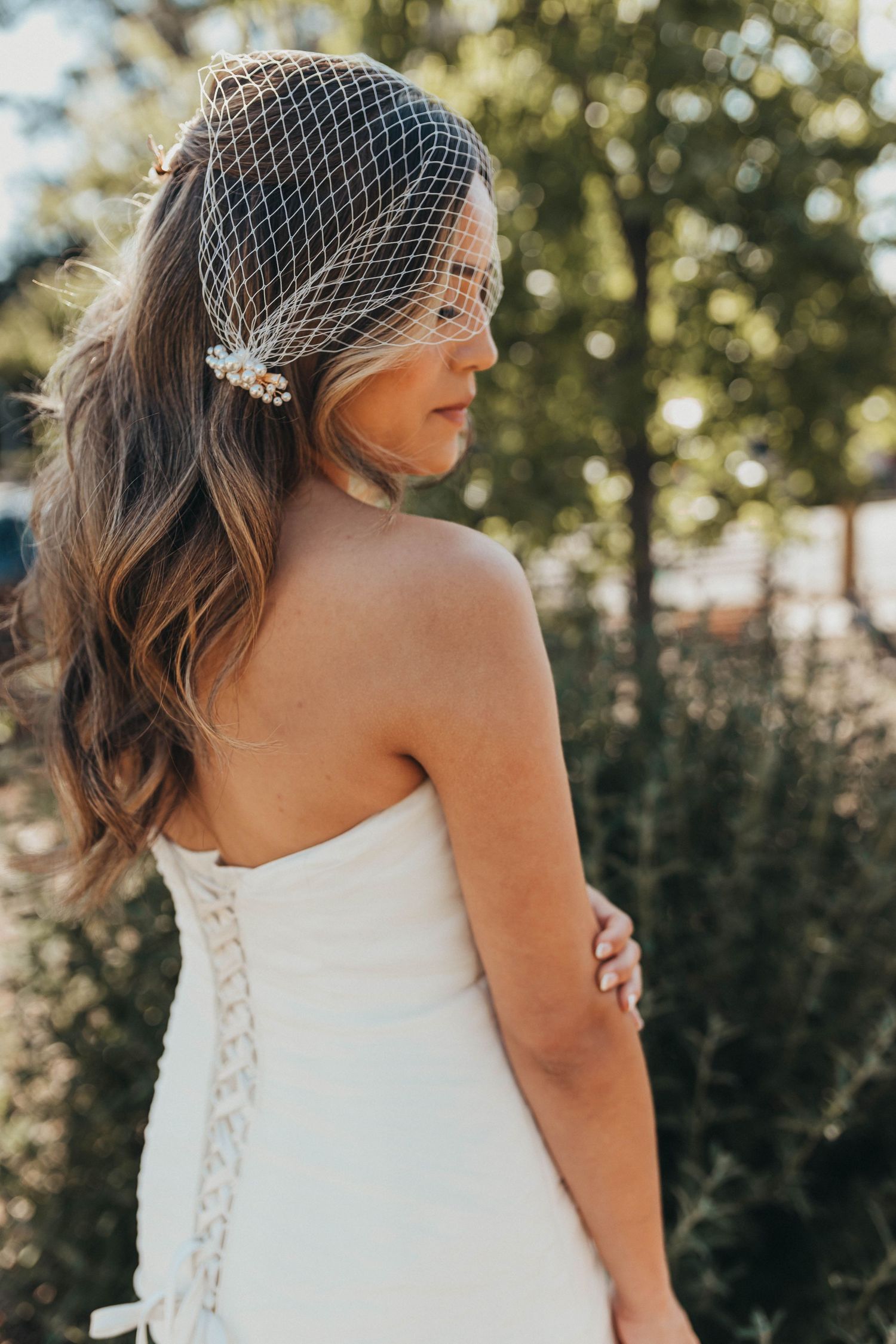 Close-up details of a white wedding dress with delicate lace-up back and soft lighting in an outdoor garden setting.