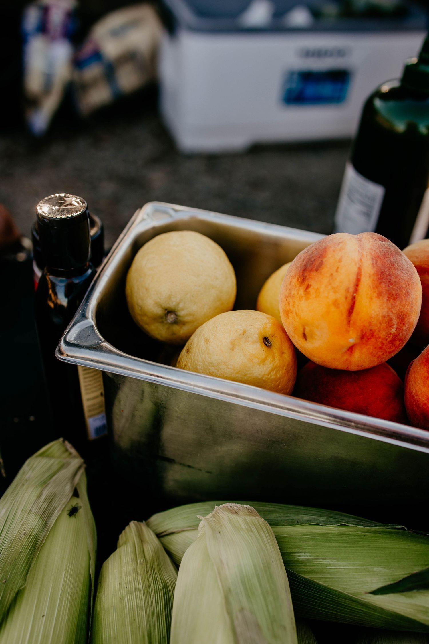 Fresh corn on the cob and peaches displayed at a farmers market or food station.