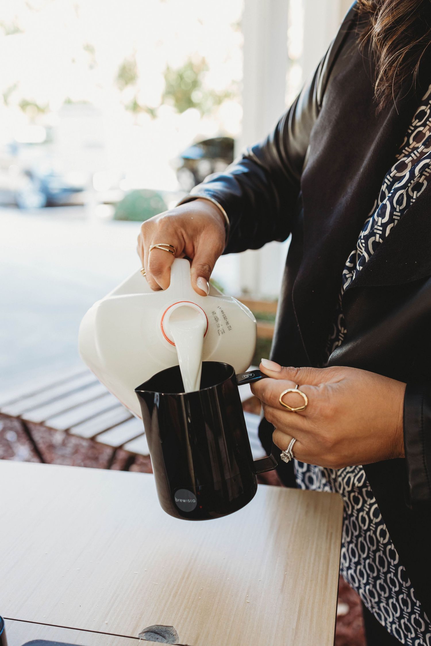 Hands pouring milk from white container into dark vessel.