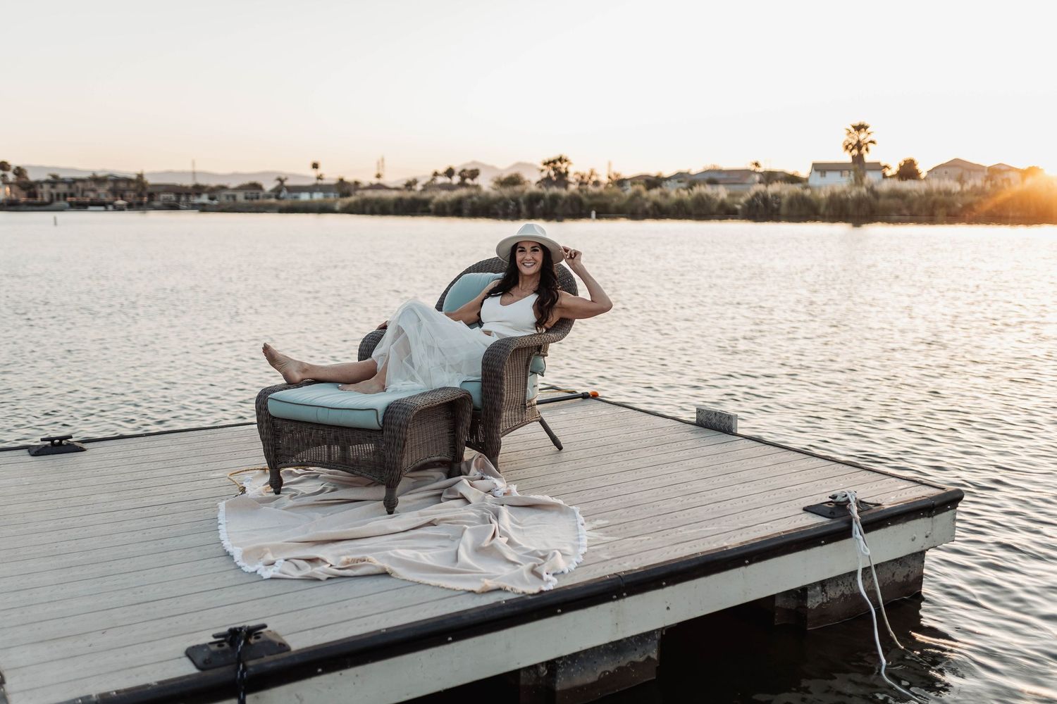 Woman relaxing in armchair on wooden dock during sunset.