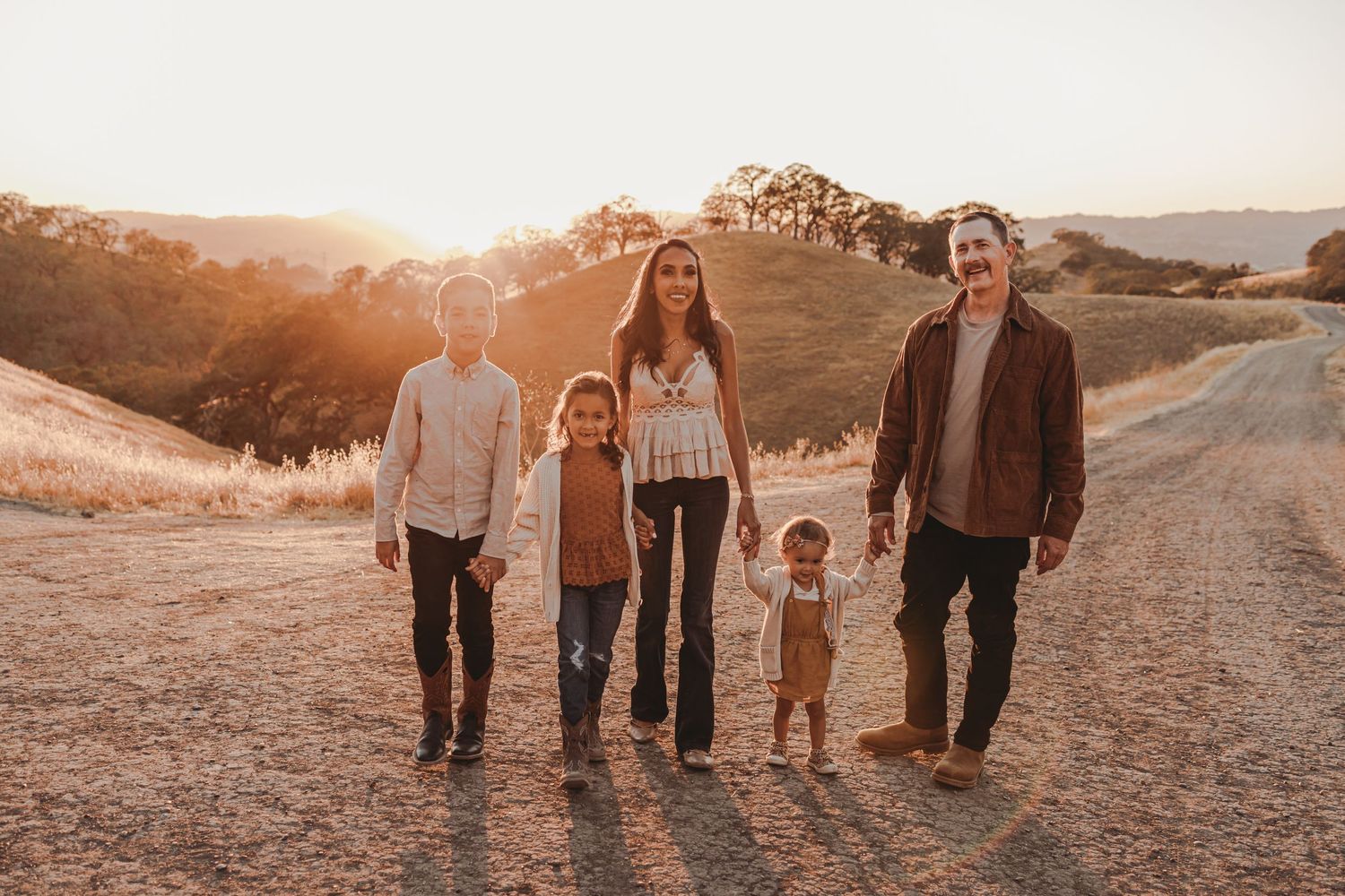 Family walking together on a dirt path at sunset in golden California hills.