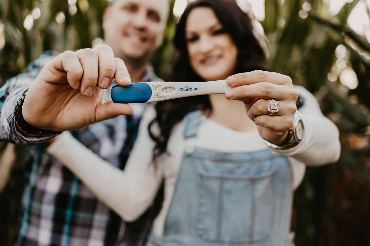 A positive pregnancy test is held up by a couple showing their excitement in an outdoor setting.