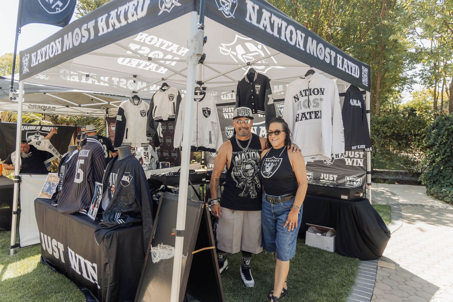 Vendors pose at Nation Most Hated Raiders fan merchandise booth outdoors.