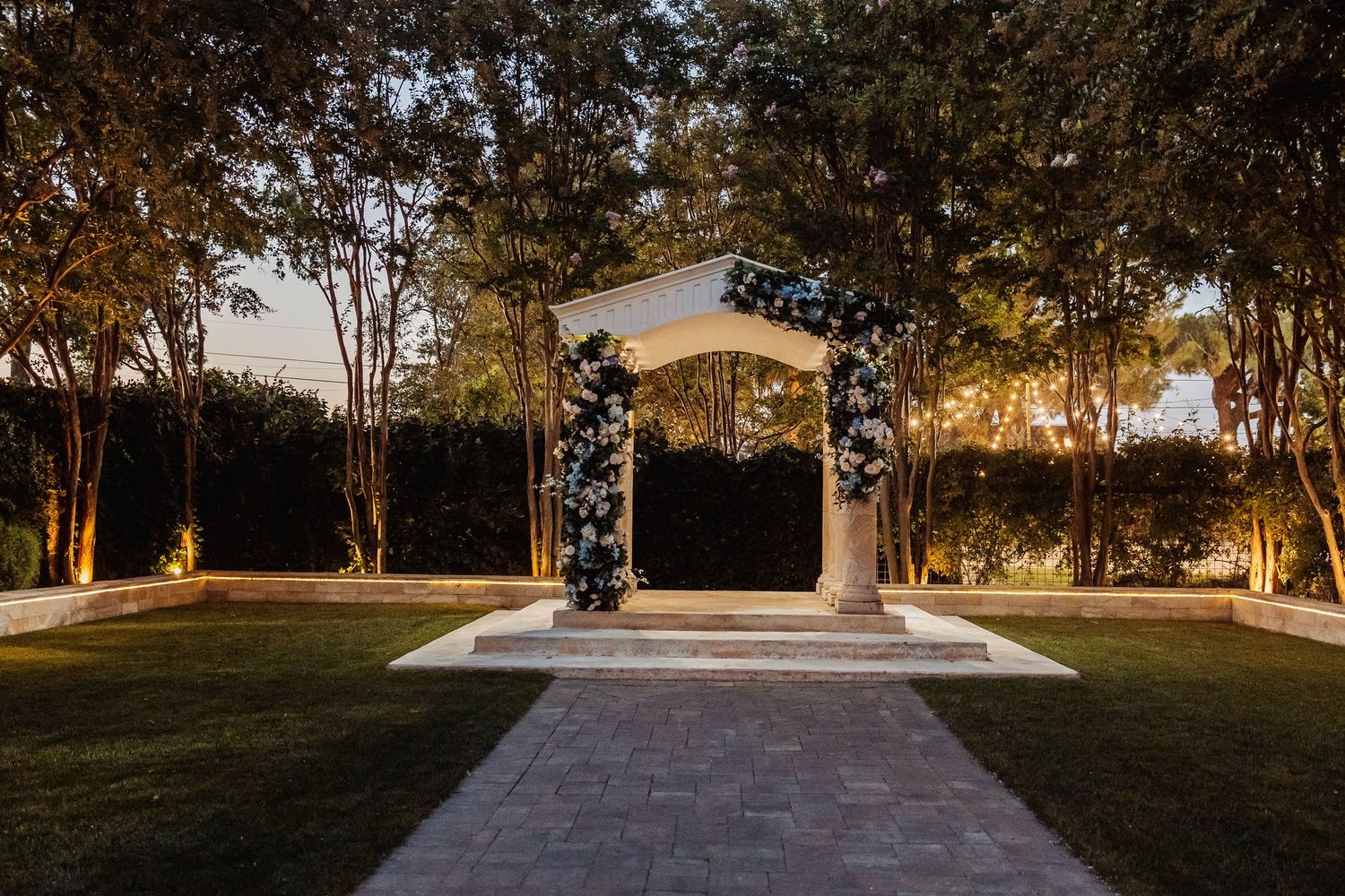 A peaceful outdoor wedding venue with white gazebo surrounded by trees at dusk.