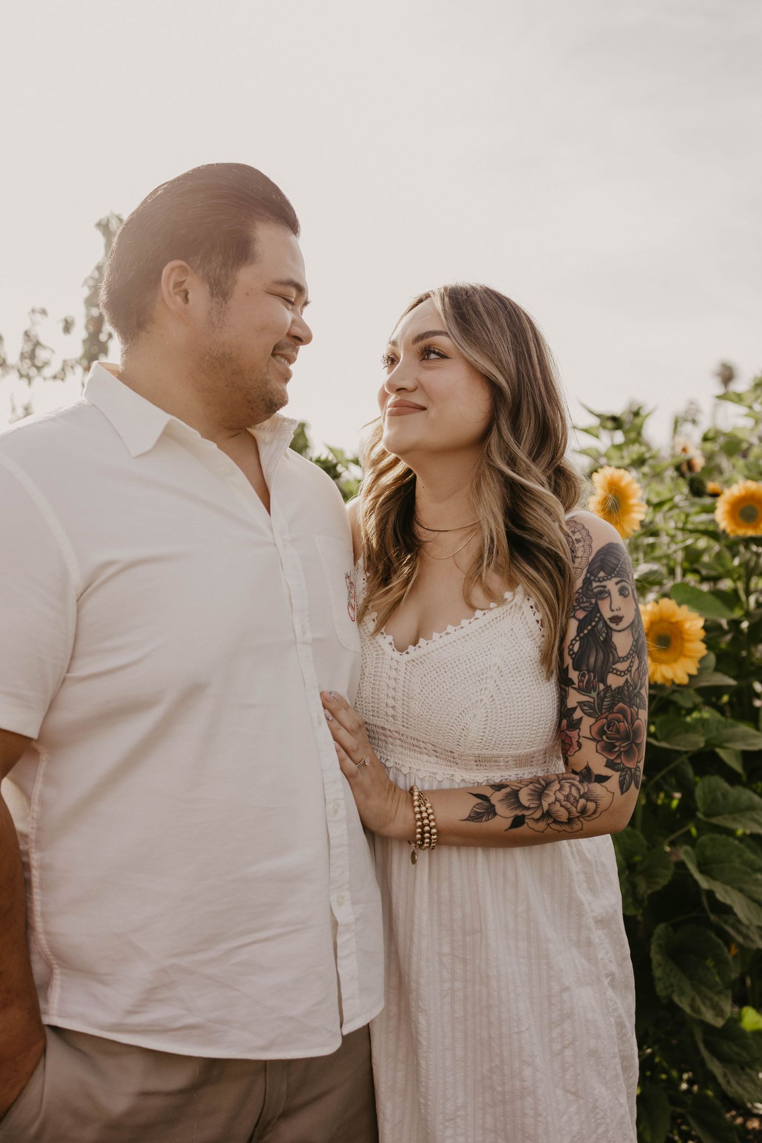 A couple in white outfits shares an intimate moment among blooming sunflowers.
