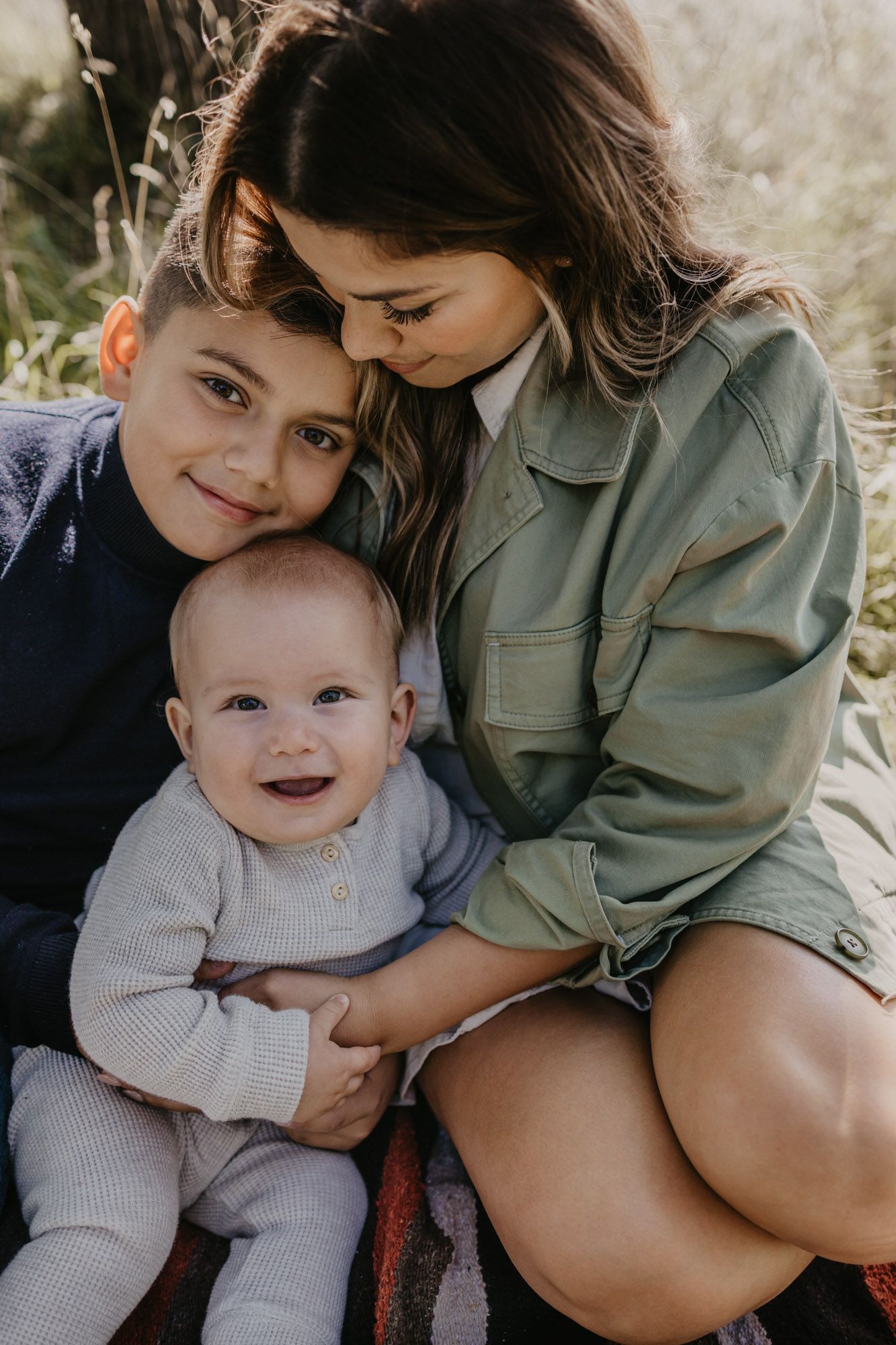 Tender family portrait showing affectionate moment between parent and children in natural setting.