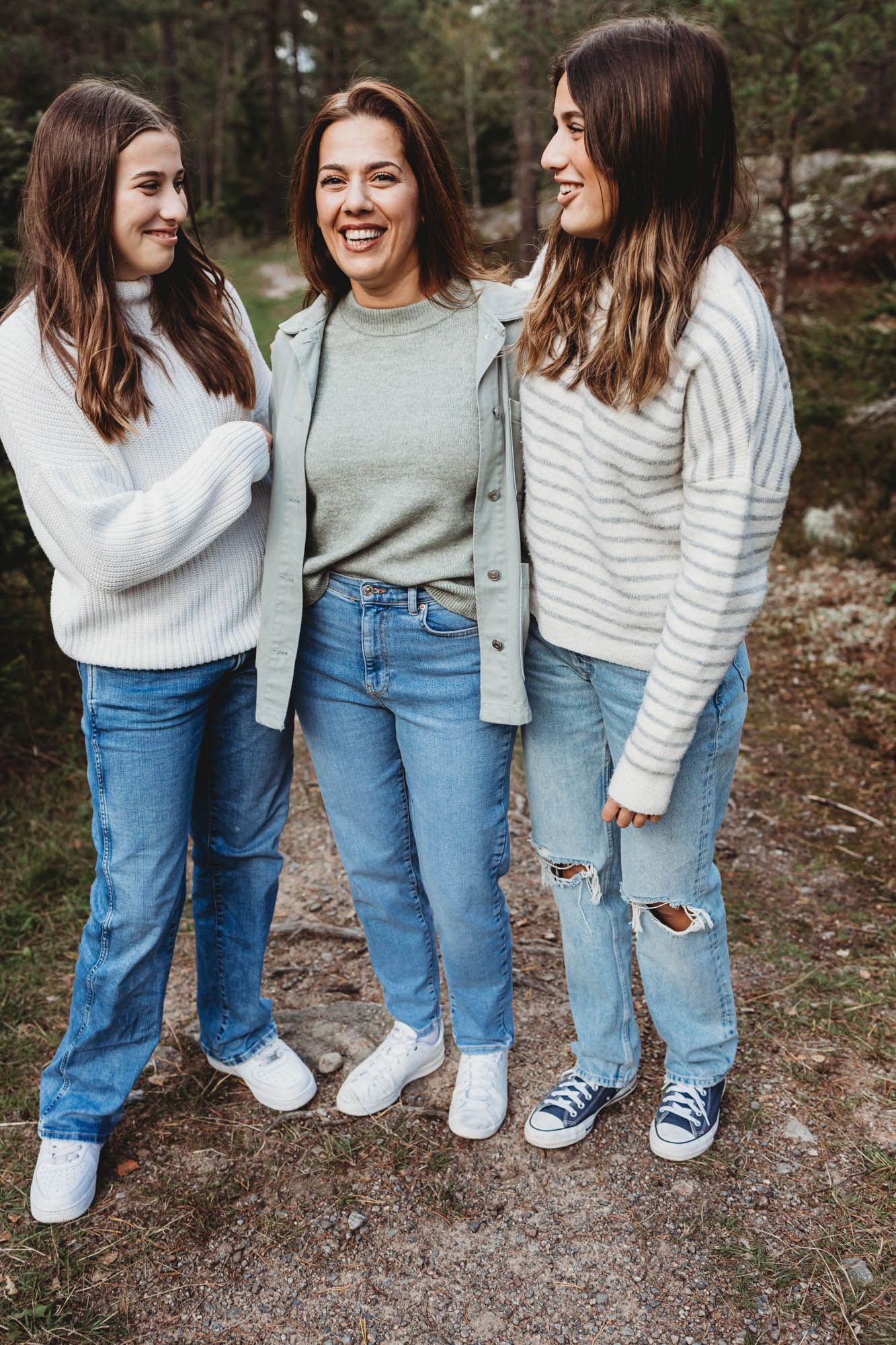 Three people in casual outfits share laughter on a forest trail.