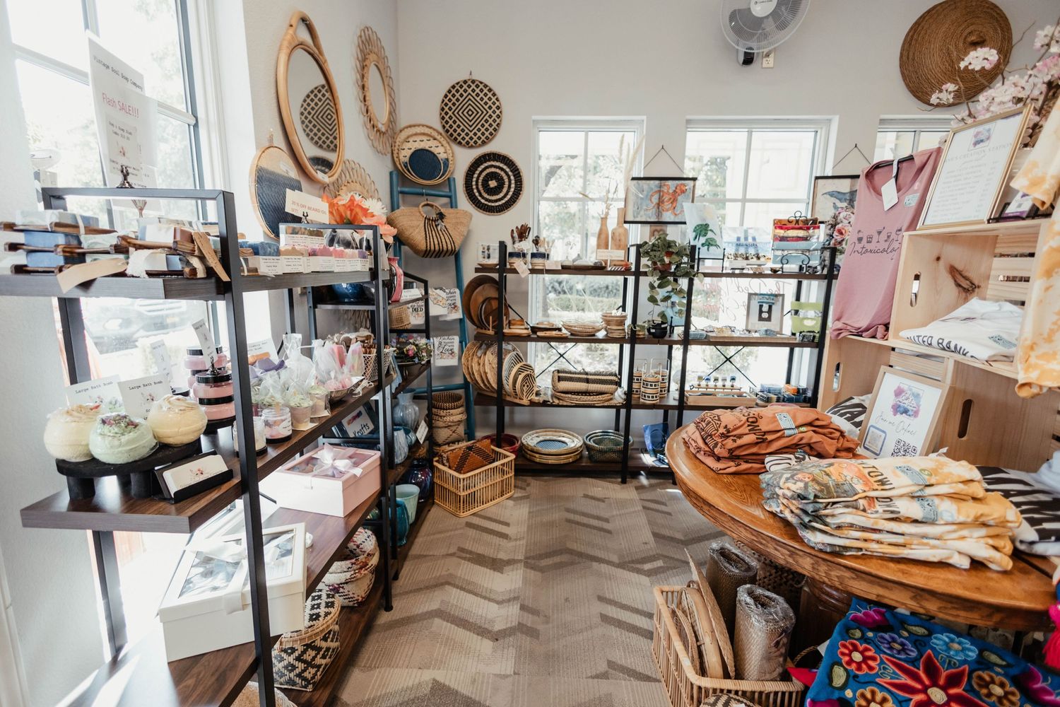 Light-filled retail space with wooden display tables and metal shelving units showcasing artisanal goods.